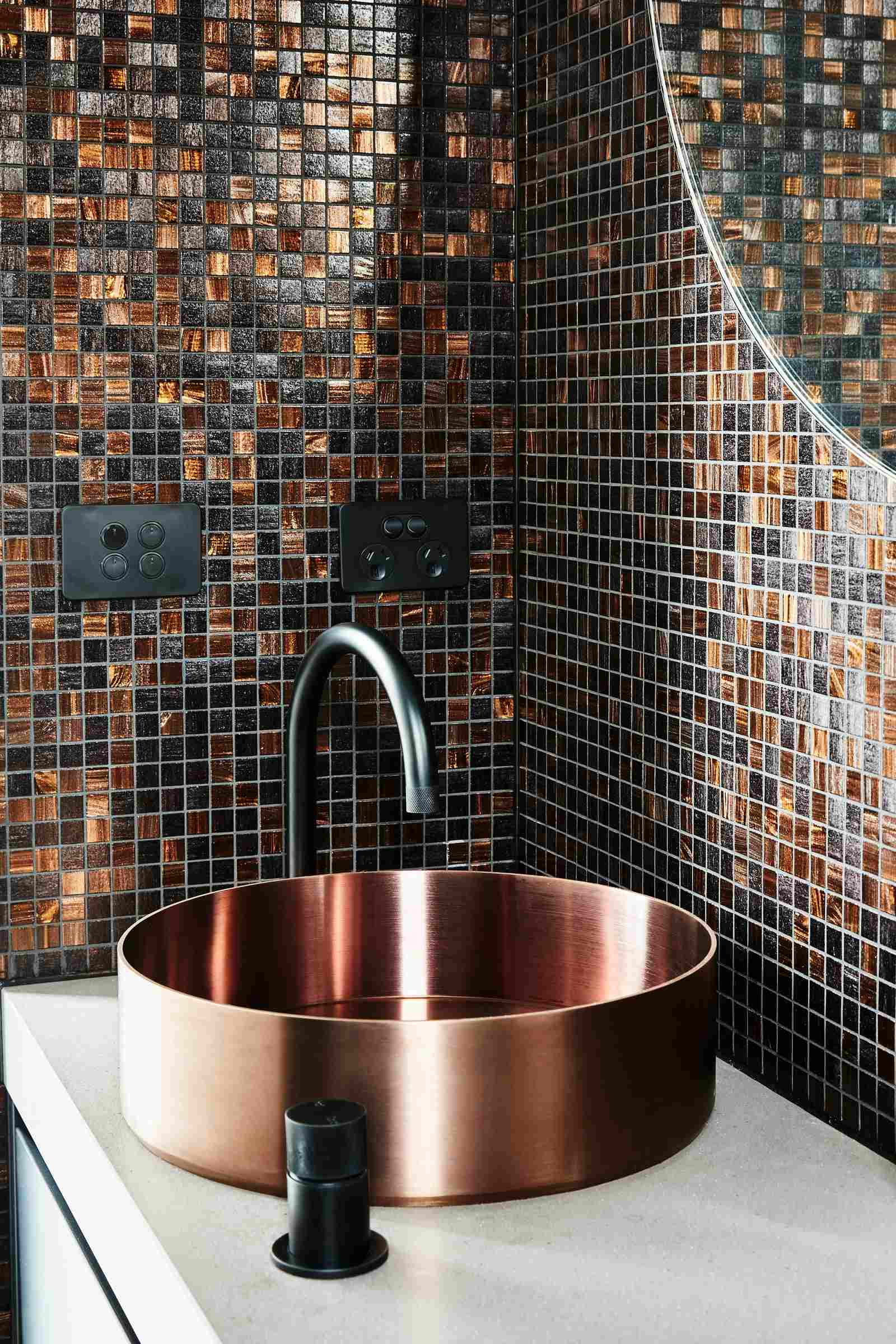 A Par Taps mixer and hob in black styled in a nice bathroom with copper basin, black and copper tile splashback and white bench