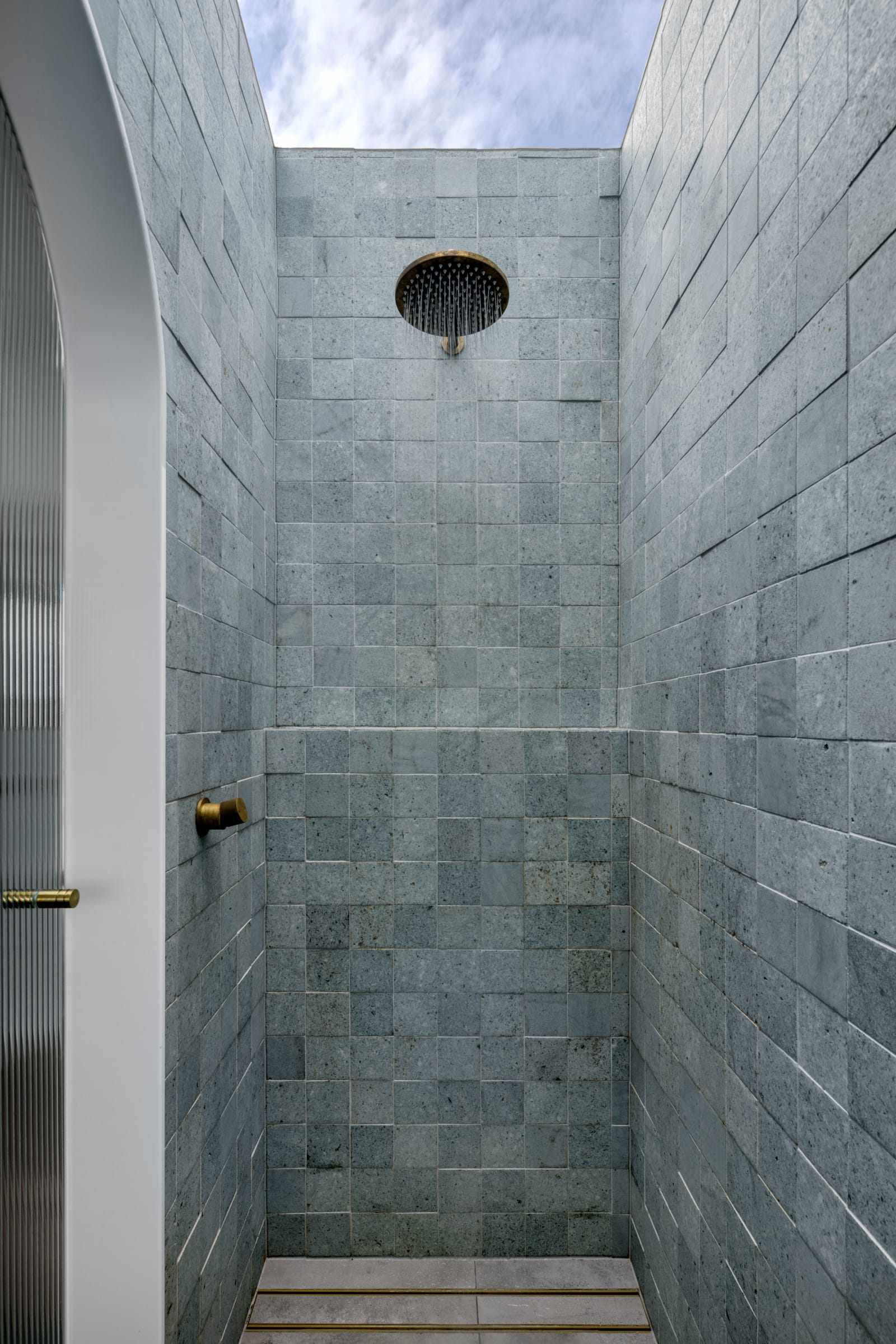A Par Taps Shower Head and Wall mixer in brass in a green tiled shower space with a skylight above