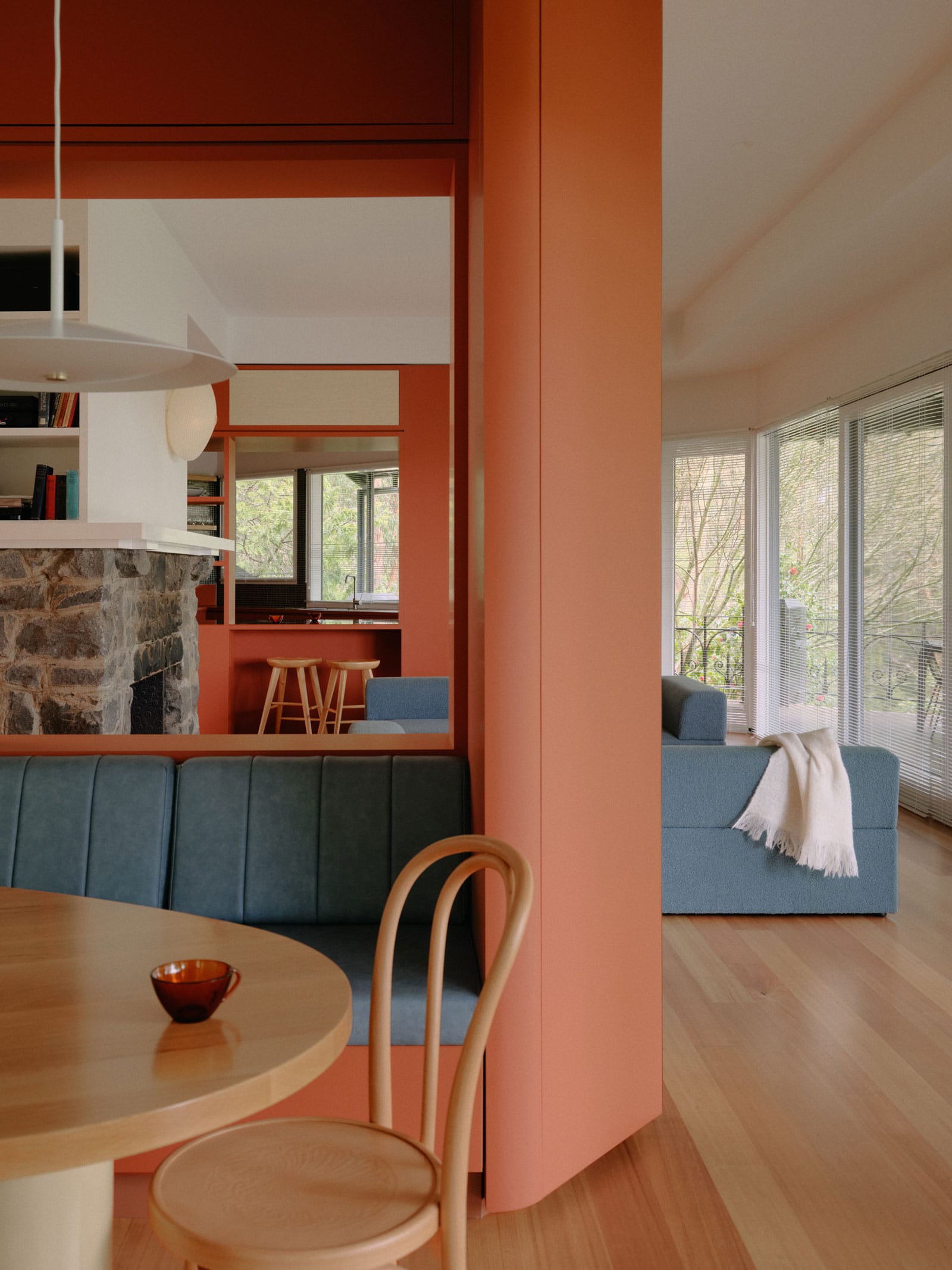 Selby House by Placement. Photography by Tom Ross. Open plan living and dining space in residential home. Timber floors. Clay coloured dividing walls and integrated cabinetry. Blue couch and bench seating upholstery.