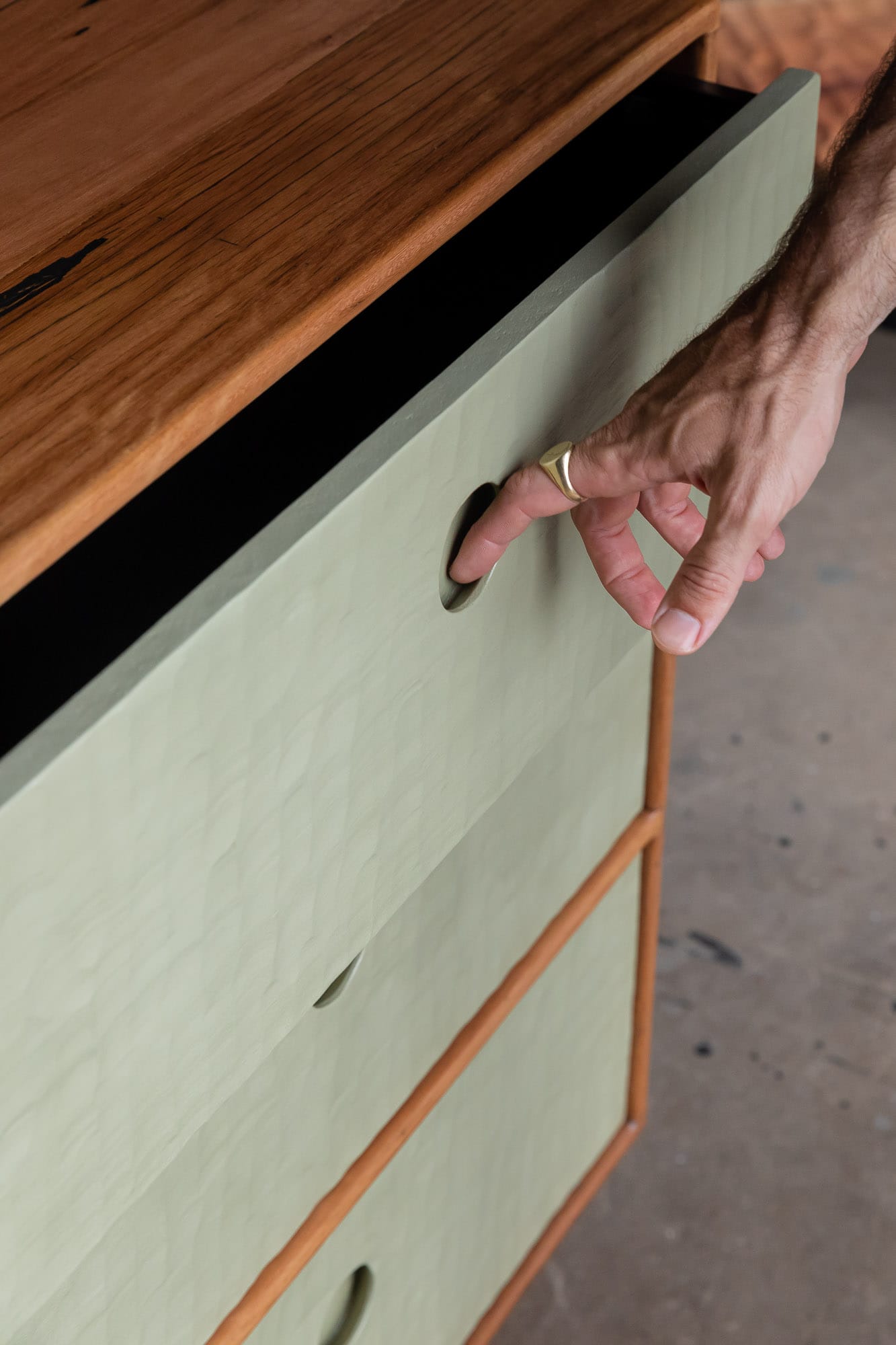 A detail shot of Two Blue Boys Furniture's set of drawers with a person pulling the drawer open using the finger pull