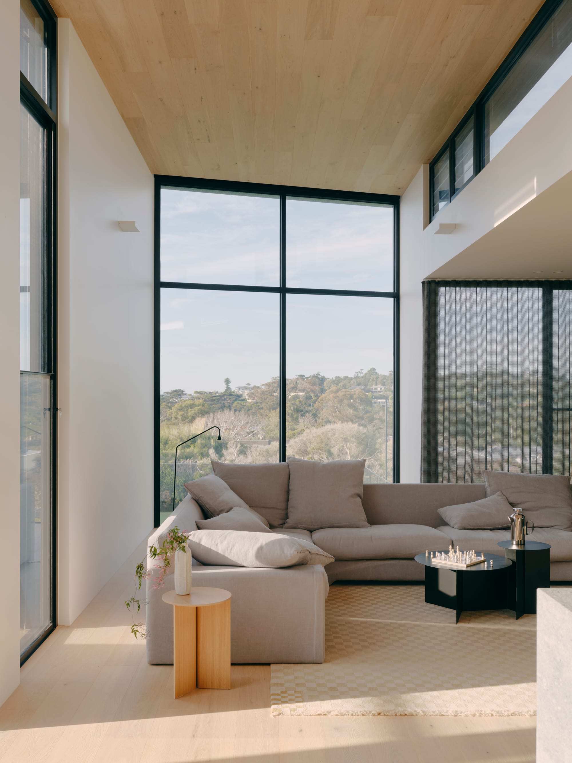 Courtside House by Tom Robertson Architects. Photography by Tom Ross. Living room with floor-to-ceiling black framed windows. Grey couch in centre of room. Light timber floors and white walls. 