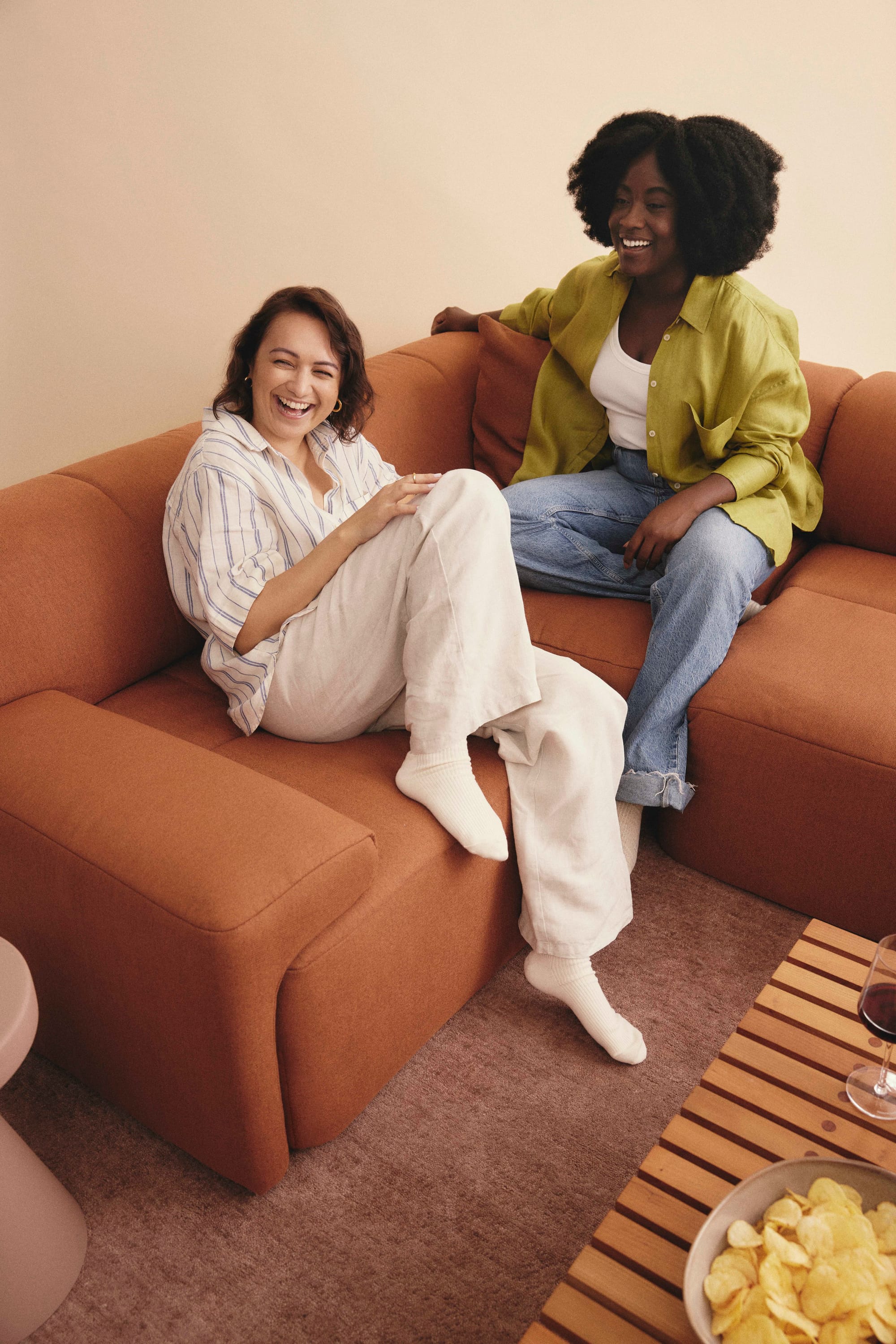 Eva Everyday Sofa. Copyright of Eva. Two young women sitting and laughing on terracotta modular lounge. 