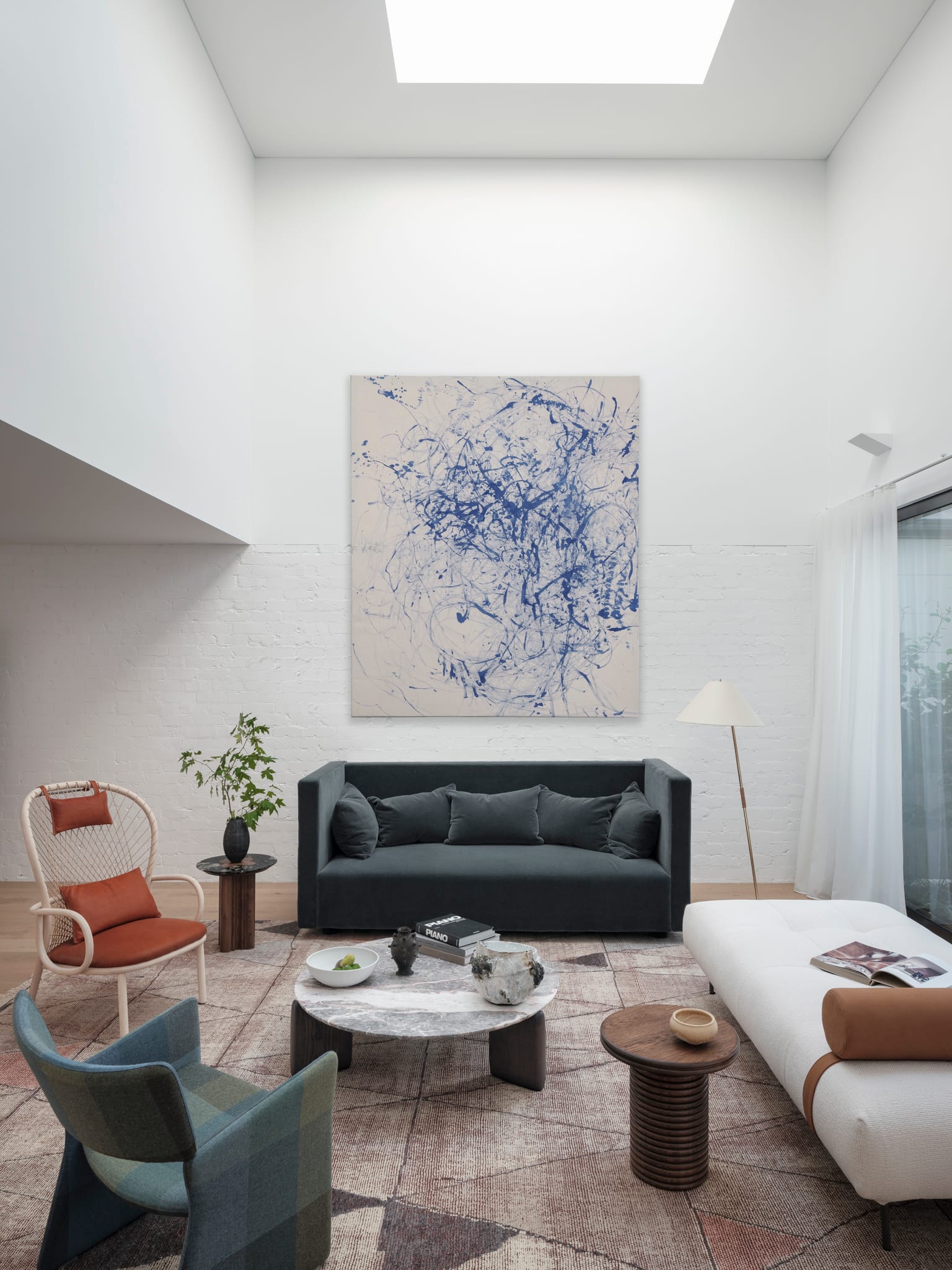 Bellevue House by Carla Middleton Architects. Photography by Tom Ferguson. Living room with overhead void and skylight. White brick wall with abstract artwork. Assorted armchairs and couches. 