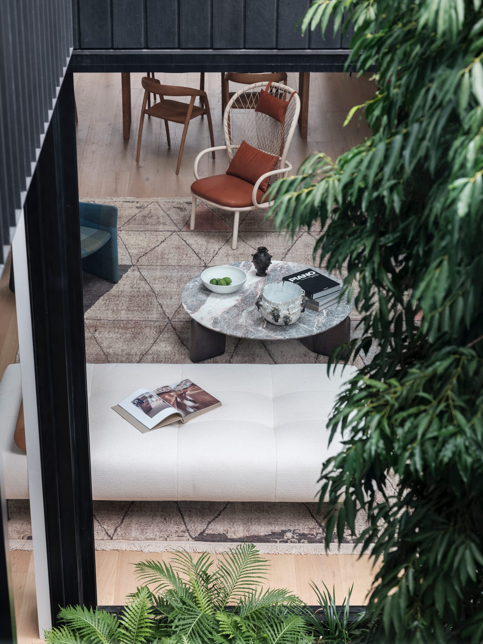 Bellevue House by Carla Middleton Architects. Photography by Tom Ferguson. Angled view from interior courtyard into interior living space. Foliage visible in foreground. Couch, coffee table and rug in background. 