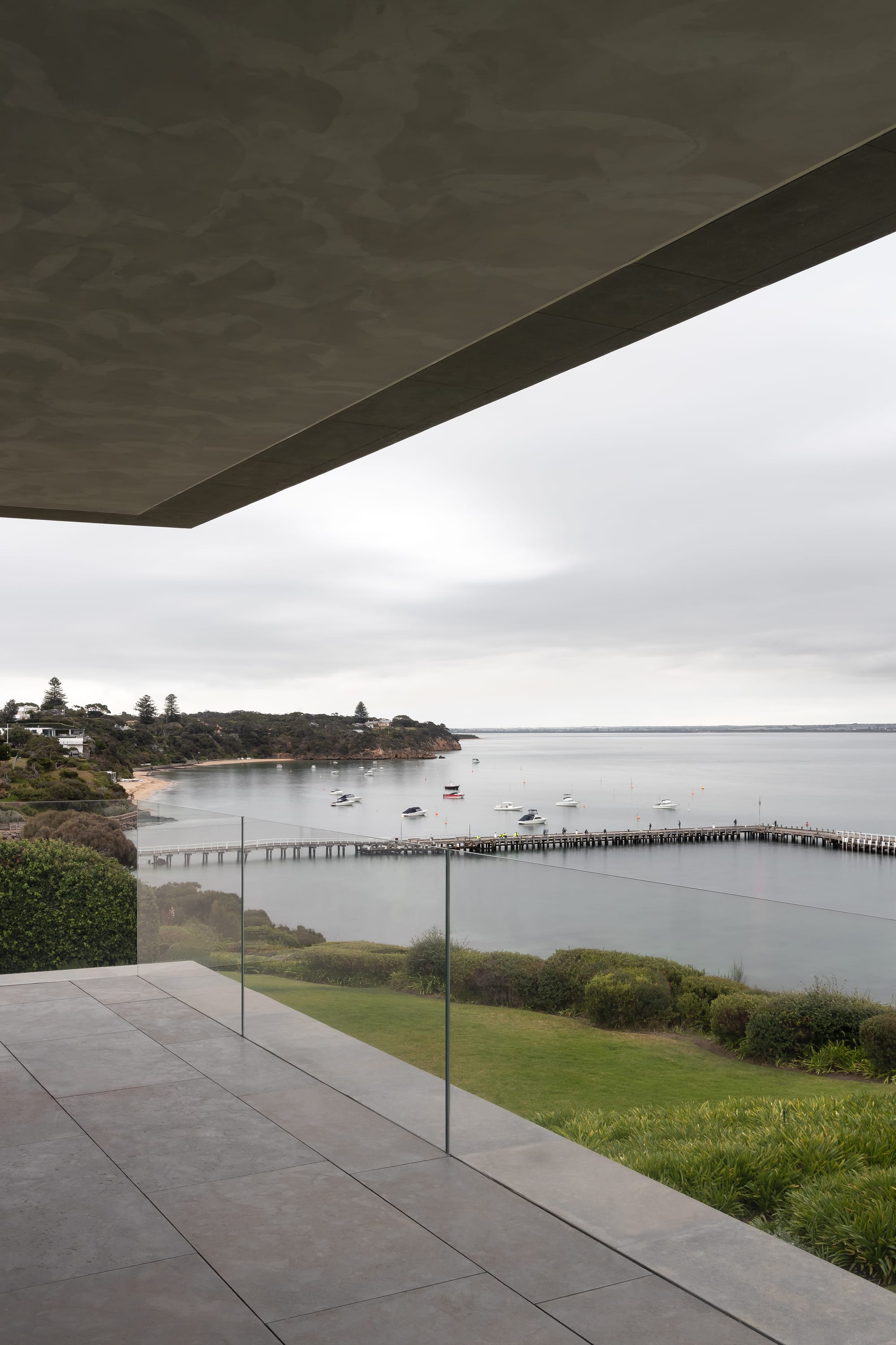Cliff House by Finnis Architects. Photography by Timothy Kaye. Views of ocean, jetty, green gardens and coastline from balcony. Stone floor and glass fence.