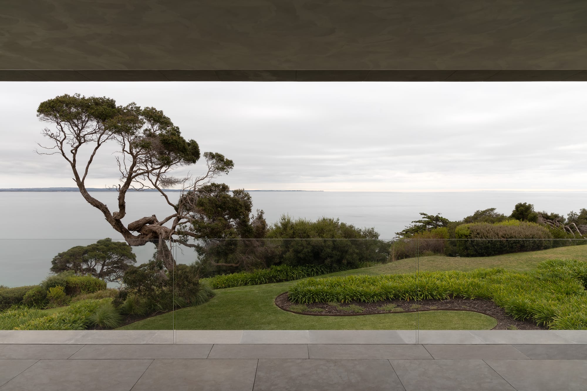 Cliff House by Finnis Architects. Photography by Timothy Kaye. View of green manicured gardens and ocean from second-storey balcony with stone flooring. 