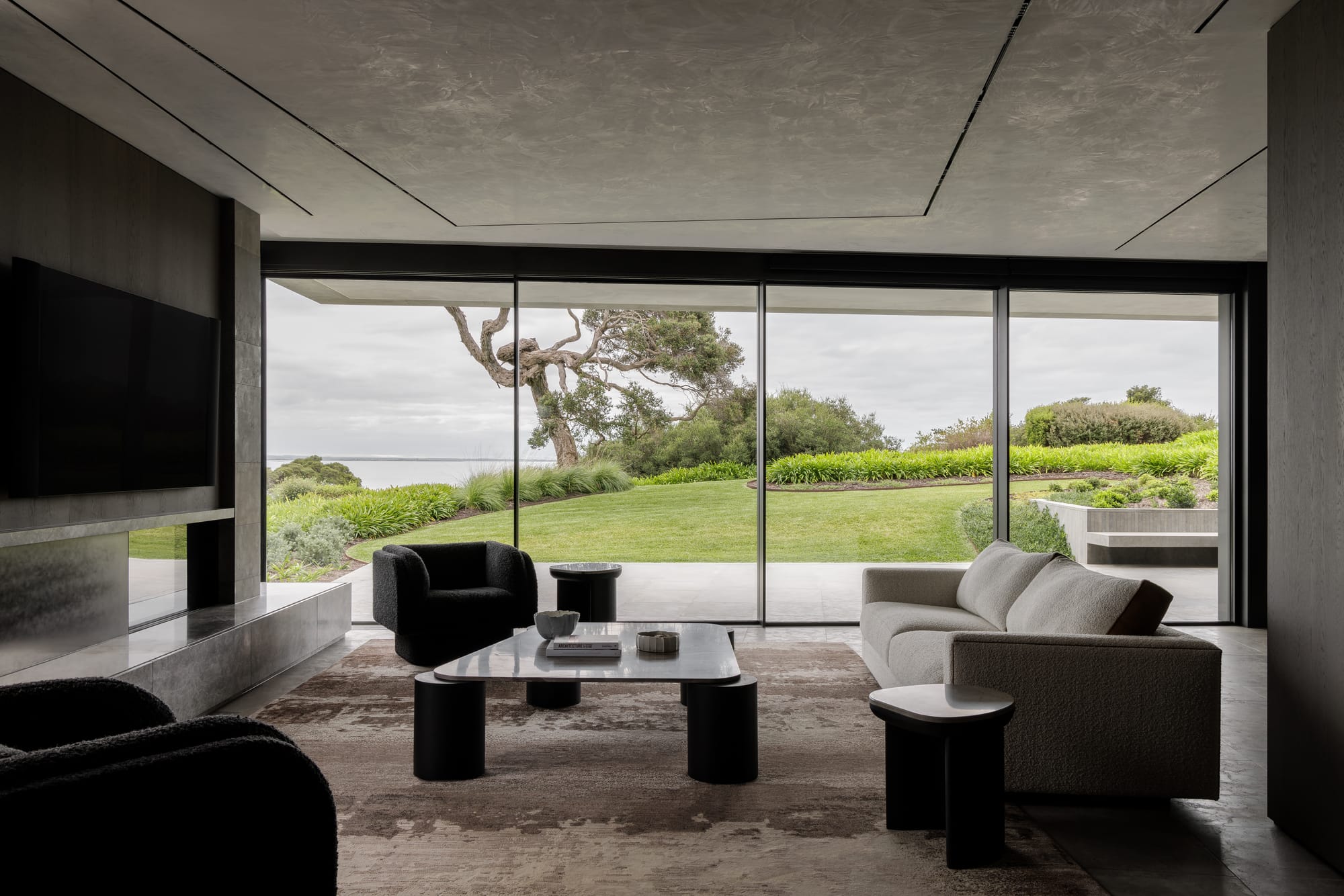 Cliff House by Finnis Architects. Photography by Timothy Kaye. Living space in front of floor-to-ceiling windows overlooking grass garden and ocean. 