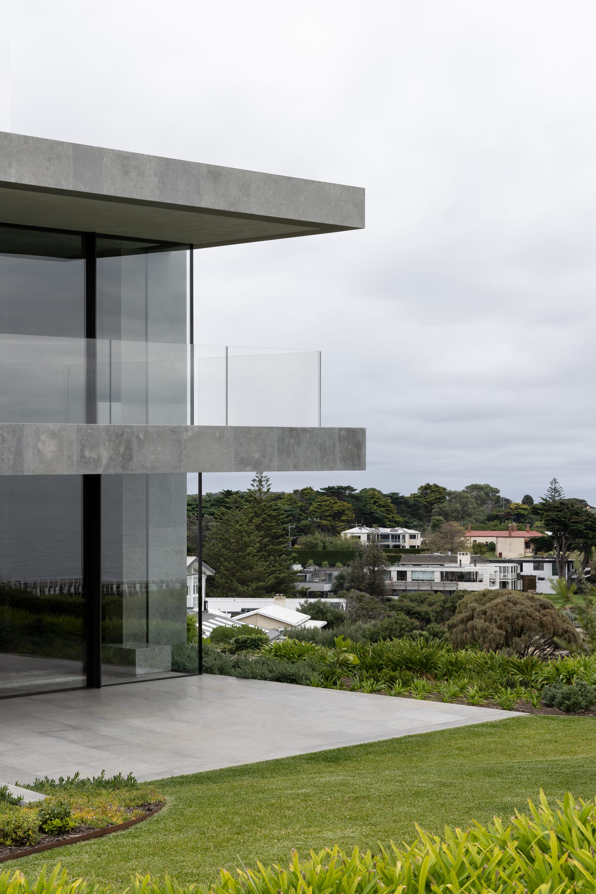 Cliff House by Finnis Architects. Photography by Timothy Kaye. Facade of contemporary double storey home with concrete finish and balcony. Floor-to-ceiling windows. Green gardens and residential views in background. 
