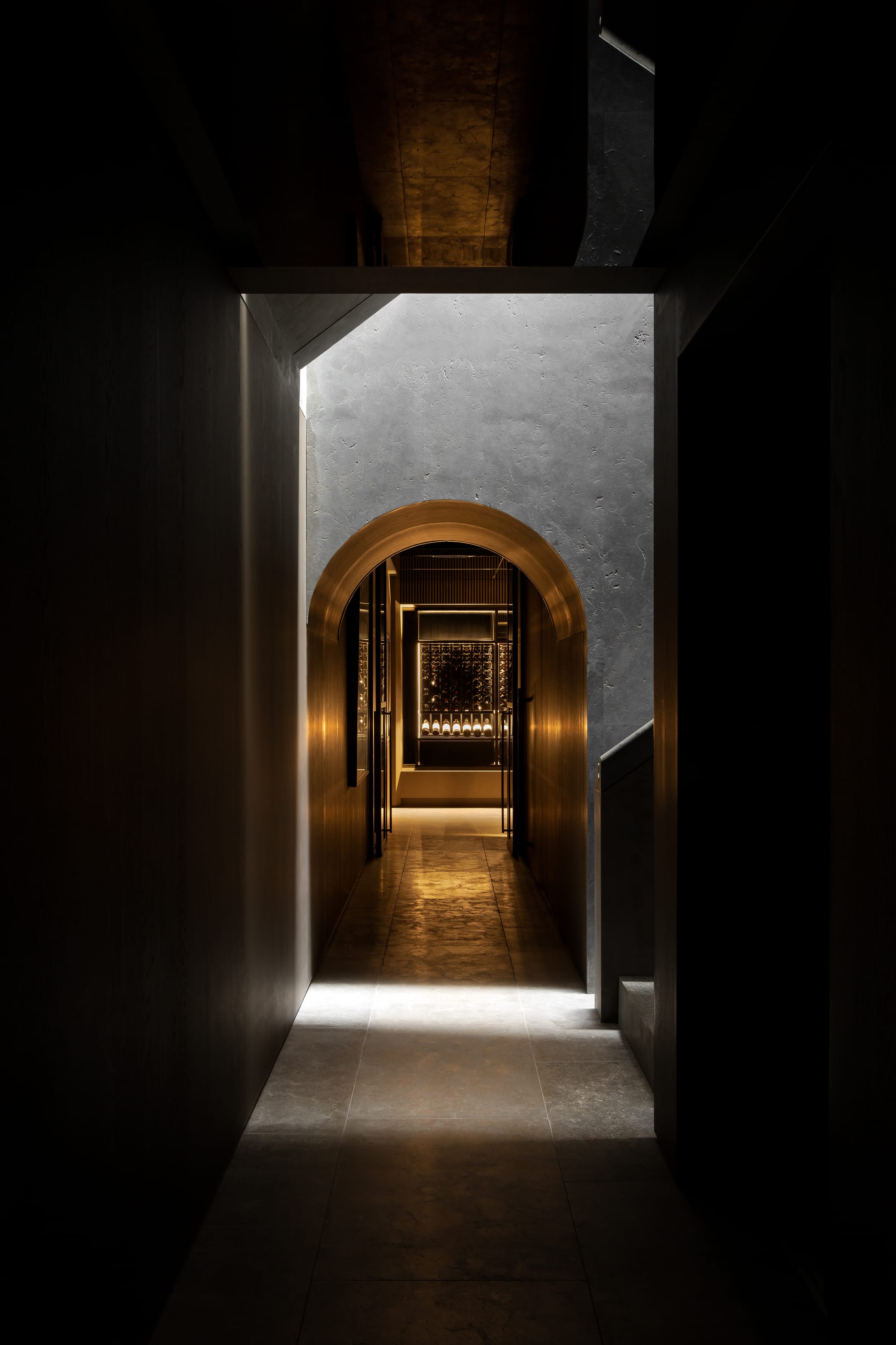 Cliff House by Finnis Architects. Photography by Timothy Kaye. Dark and moody hallway with warm light at end. Stone floors and walls with archways. 
