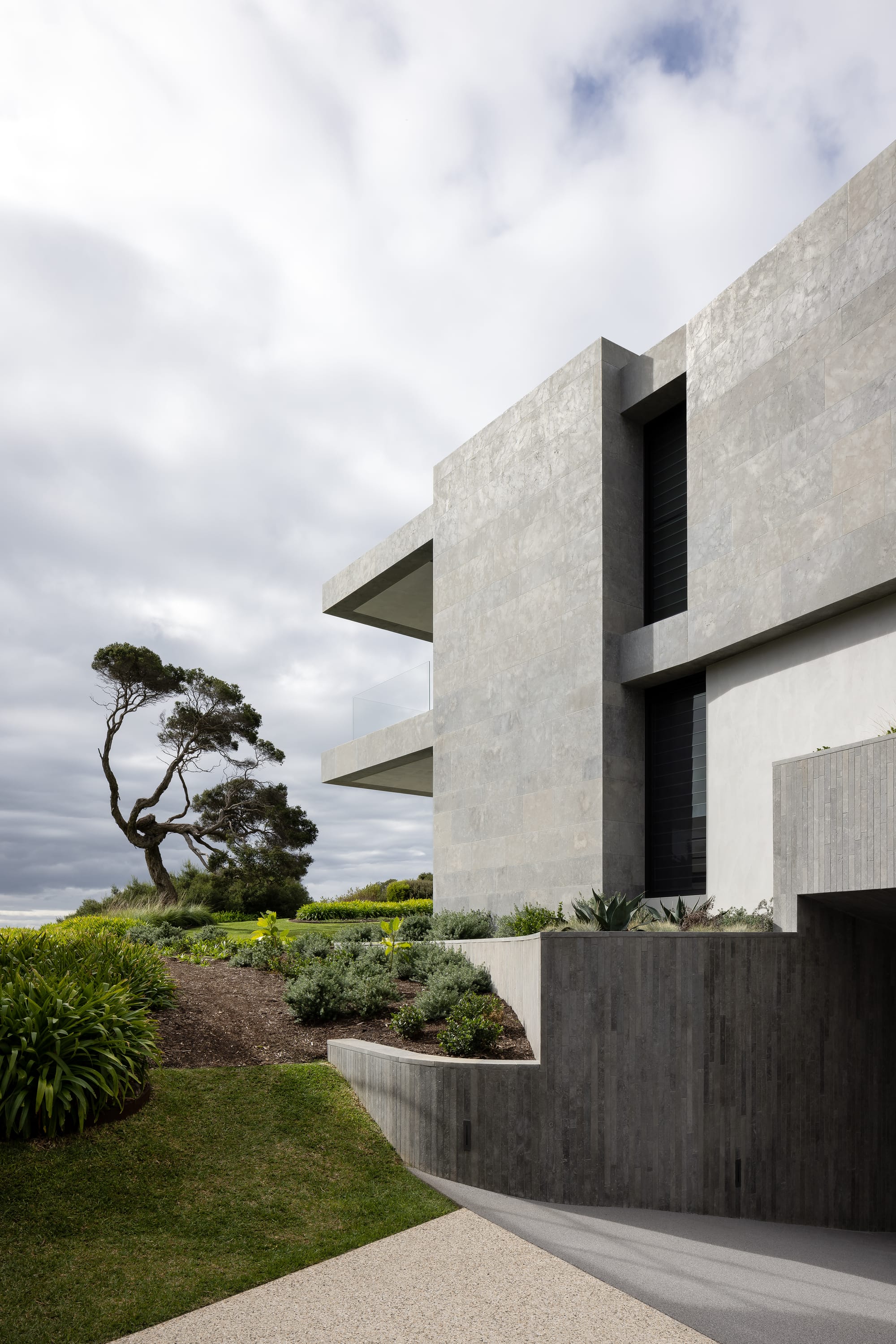 Cliff House by Finnis Architects. Photography by Timothy Kaye. Exterior facade of contemporary home with concrete finish and rolling gardens meeting sides of home. 