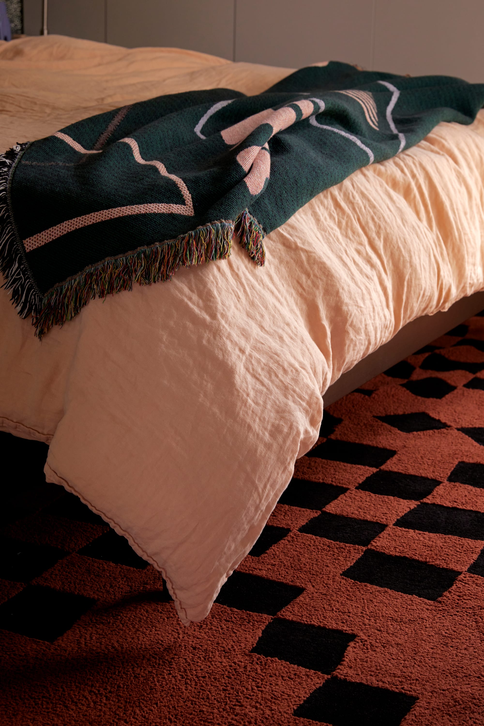 Checking Brown Cotton Feel Rug by Double. Photographer: Jacqui Turkc. Terracotta and black checkered rug. Peach linen bed cover with bottle green throw rug on end of bed. 