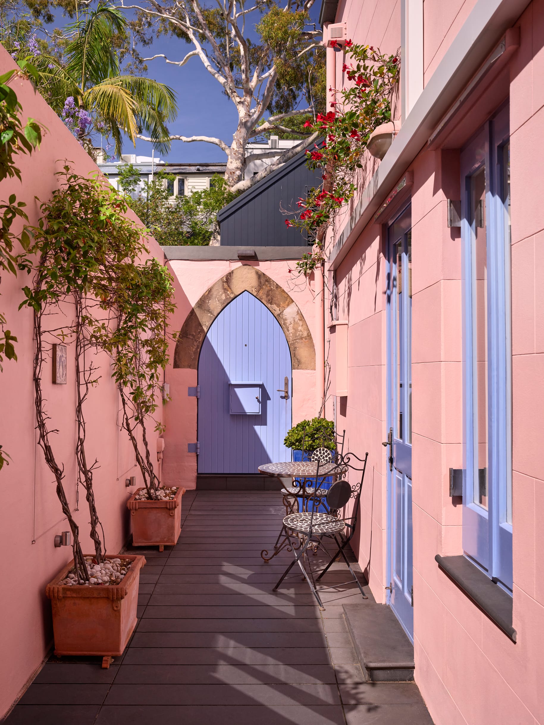 Chapel House by FURNISHD. Photography by Alicia Taylor. Patio with pink walls and blue window frames. Blue arched door. Dark flooring and plants growing up walls. 