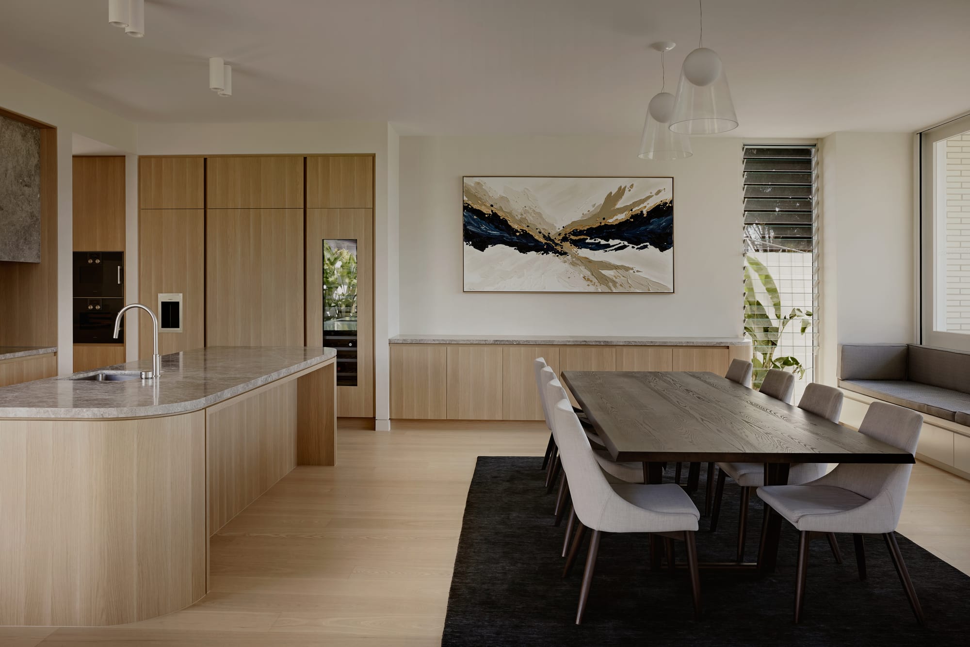 Hill Courtyard House by Kelder Architects. Photography by Brock Beazley Photography. Kitchen and dining area with timber floors, benches and joinery. Dark timber table with white chairs on black rug. Abstract painting. 