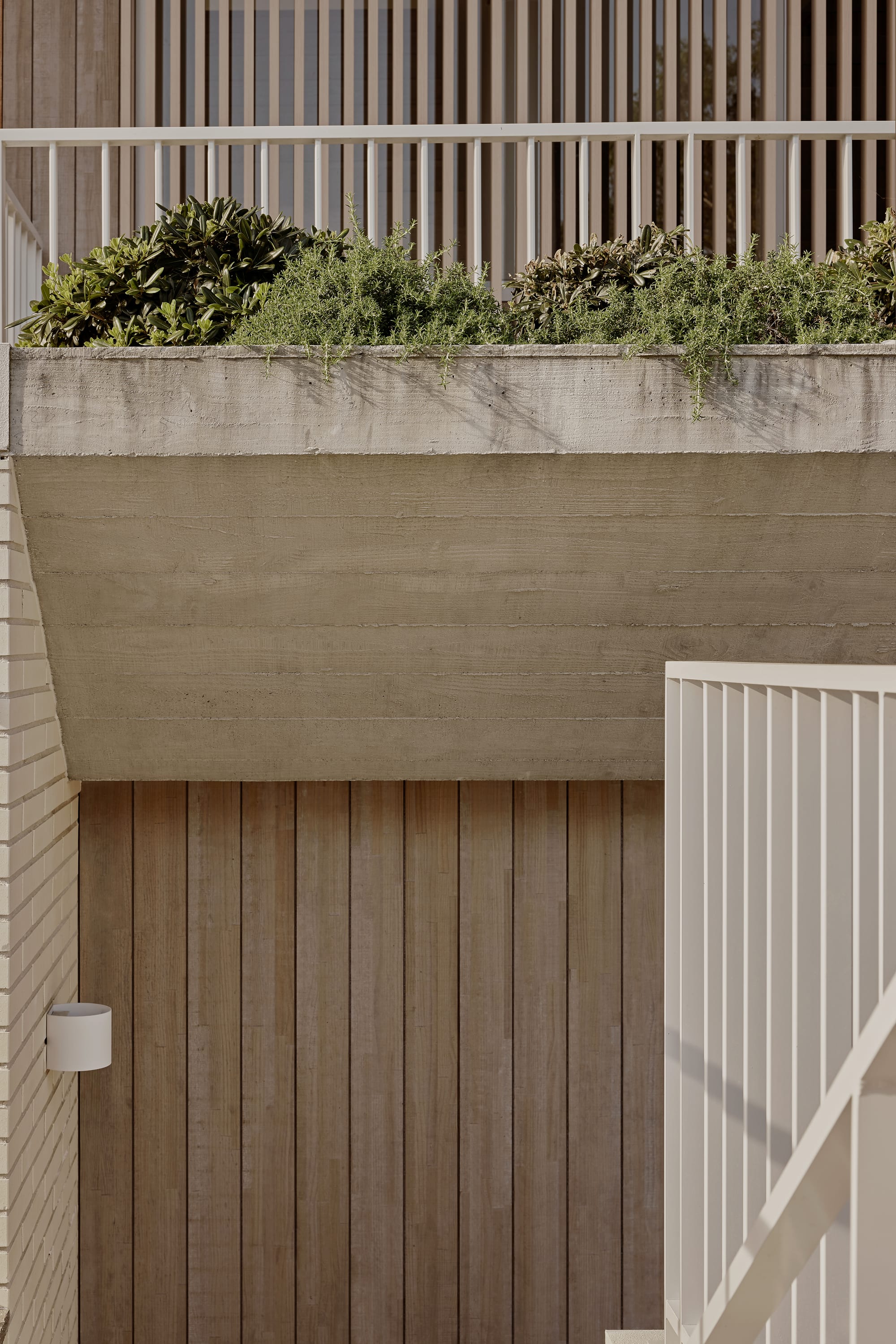  Hill Courtyard House by Kelder Architects. Photography by Brock Beazley Photography. Close up of timber garage door with concrete garden bed above. white railing for balcony behind garden bed. 