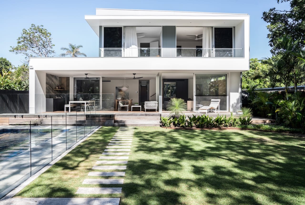 Kasa Byron Bay. Copyright of Kasa Byron Bay. Rear facade of contemporary double storey home finished with white render. Grass with paved footpath, and pool on the left. 