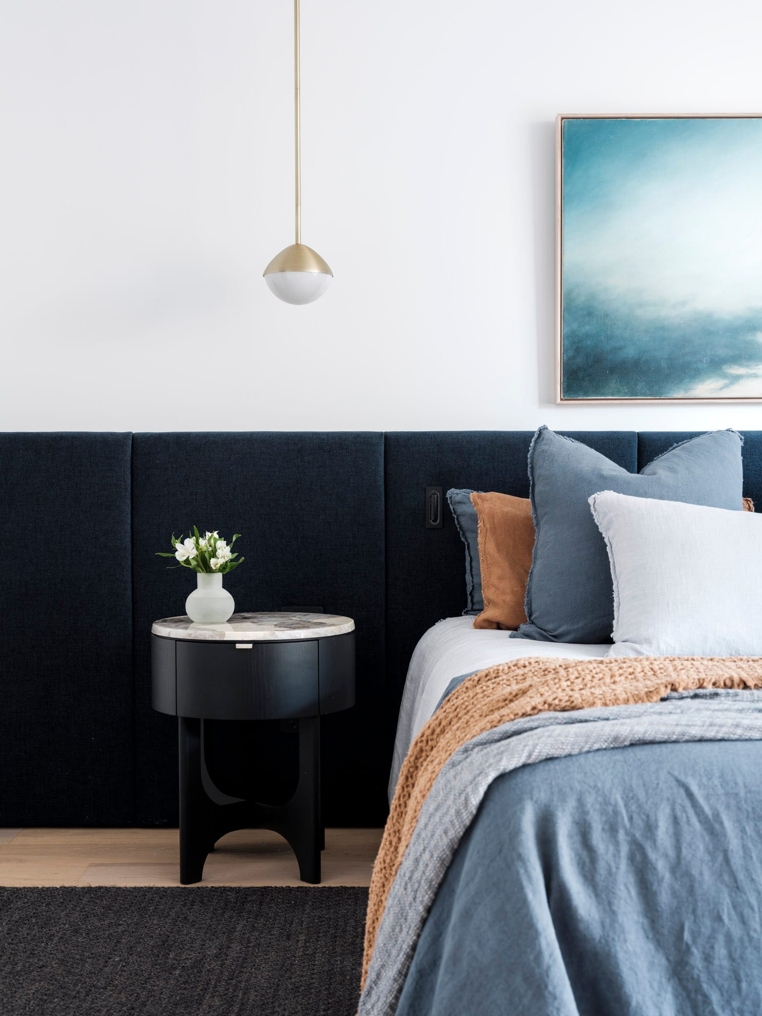 Kasa Byron Bay. Photography by Tom Ferguson. Bedroom with built in navy upholstered bedhead running length of room. Timber floors. Black bedside table. Blue bed linen.