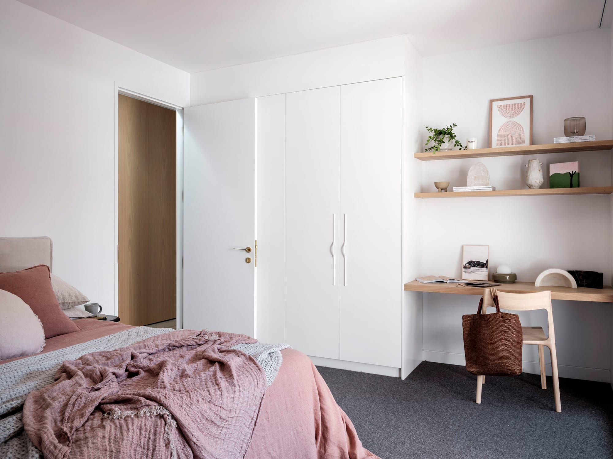 Kasa Byron Bay. Photography by Tom Ferguson. Bedroom with grey carpet, white walls and cabinetry and timber floating desk nook. Bed with pink linen to left. 