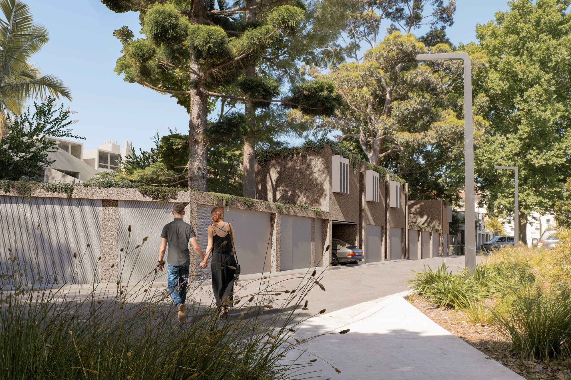 Nobbs Lane by Studio Shand. Imagery by Dan Layden. Couple walking along footpath inbetween tall trees and lush garden beds. Small, contemporary units visible further up the pathway. 
