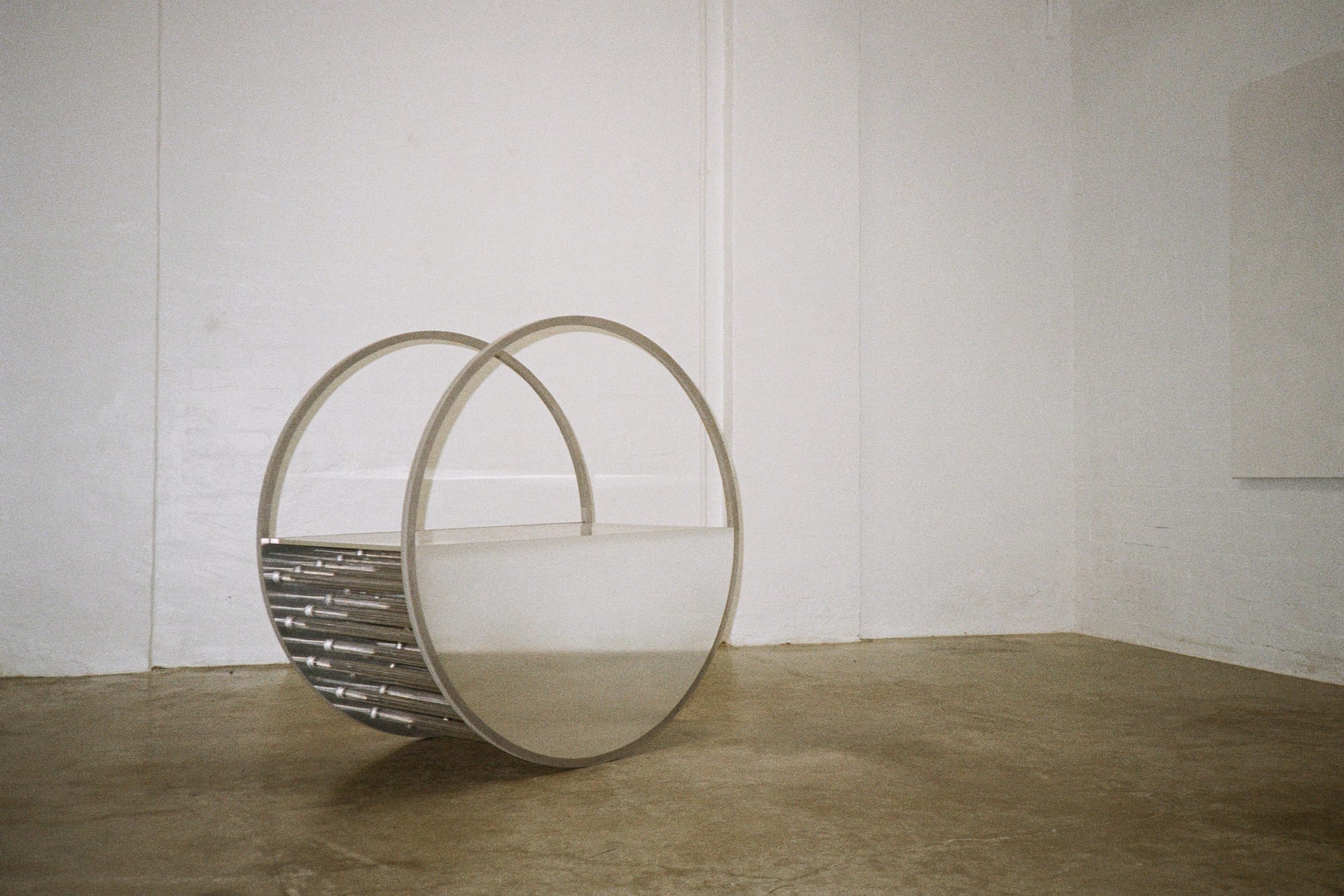 Array 11 by Studio Shand. Photography by Benjamin Jay Shand. Circular sculpture. Barren room with white walls and concrete floor. Curved chrome makes hollow 3D circle sculpture. 