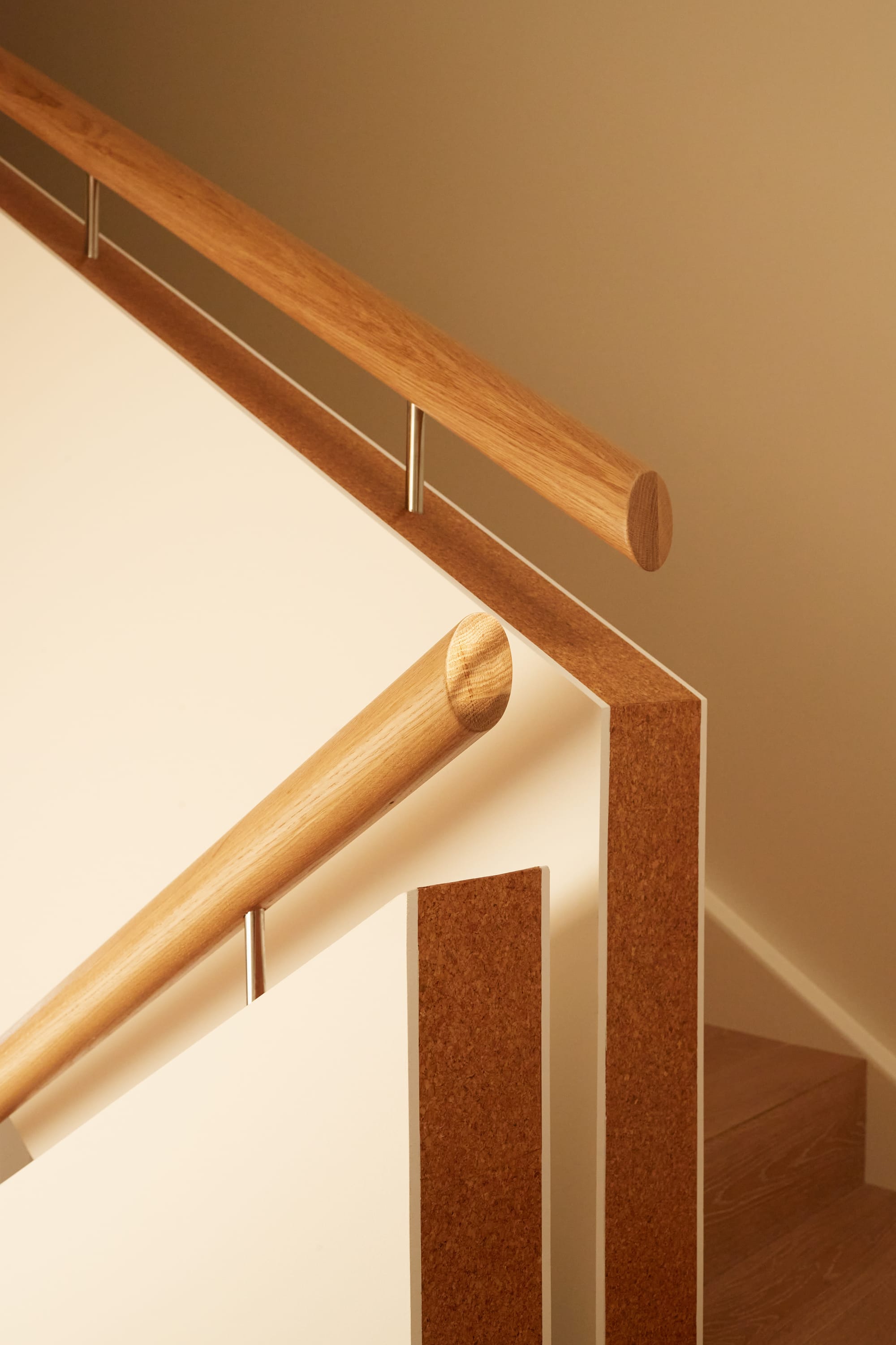 Cork House by Studio Shand. Photography by Traianos Pakioufakis. Close up of staircase. White walls with cork inner. Timber handrail and steps. 