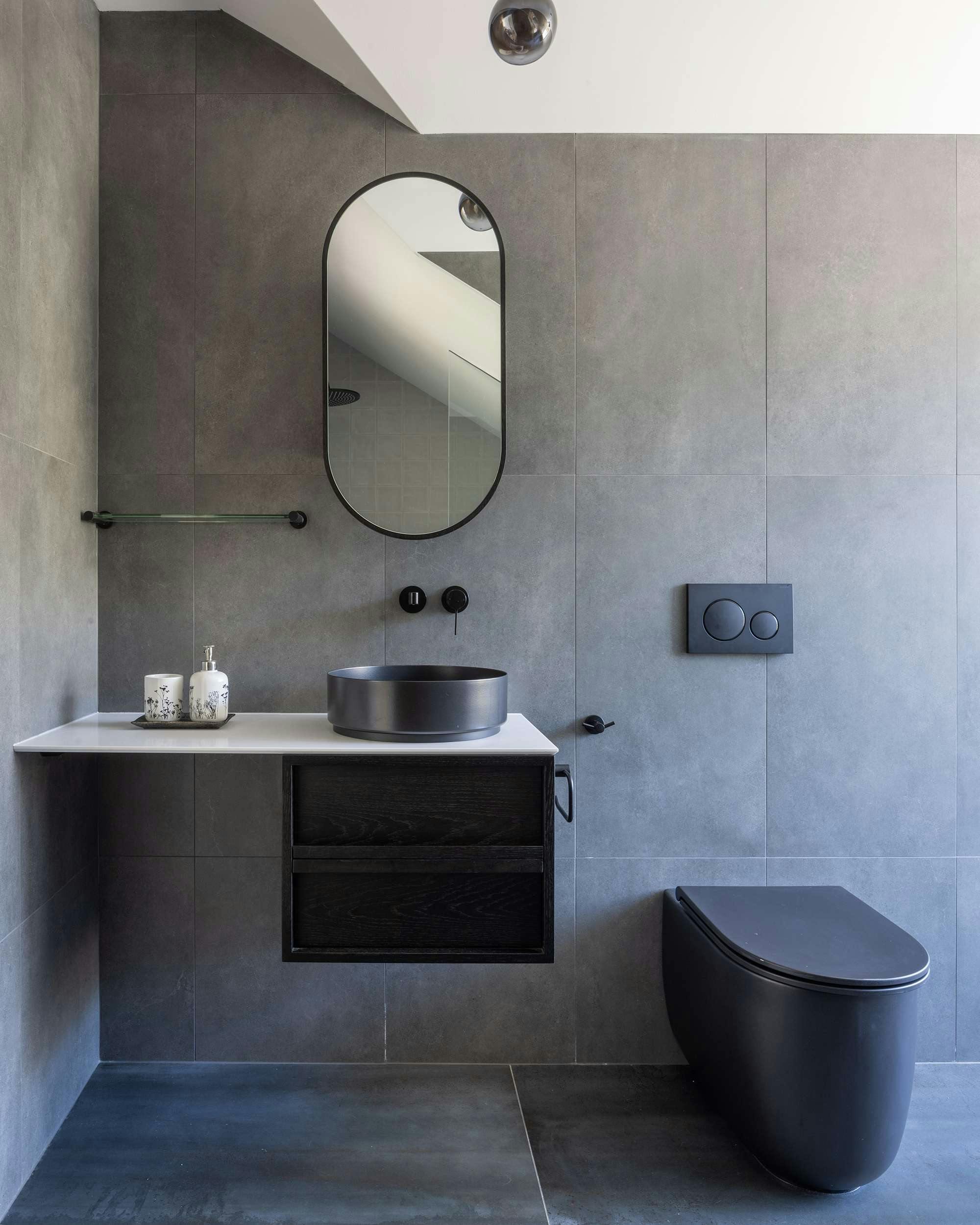 An interior shot of the new ensuite with black fixtures and a round mirror above a basin