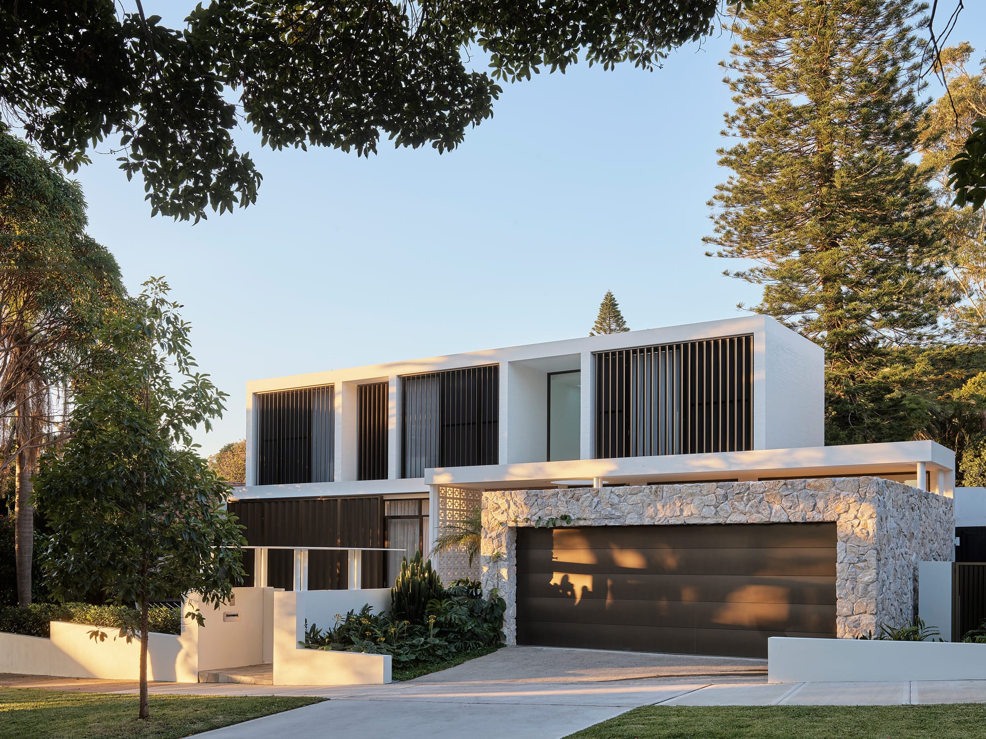 Warren House by CM Studio. Photography by Nic Gossage. Street view of contemporary double storey home with stone wall around garage roller door. 