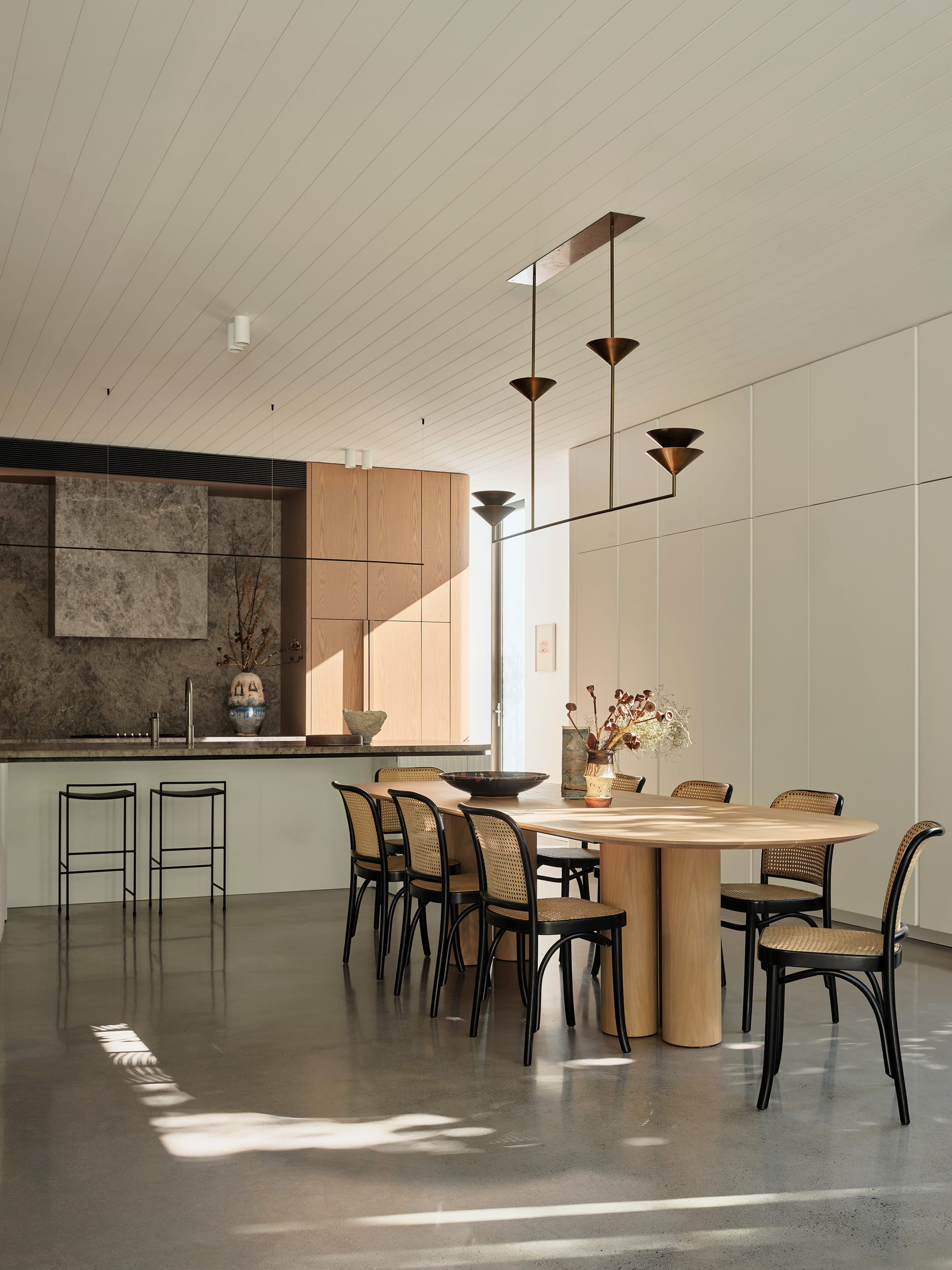 Warren House by CM Studio. Photography by Nic Gossage. Open plan dining and kitchen with polished concrete floors and integrated cabinetry. Timber table and kitchen cupboards. 