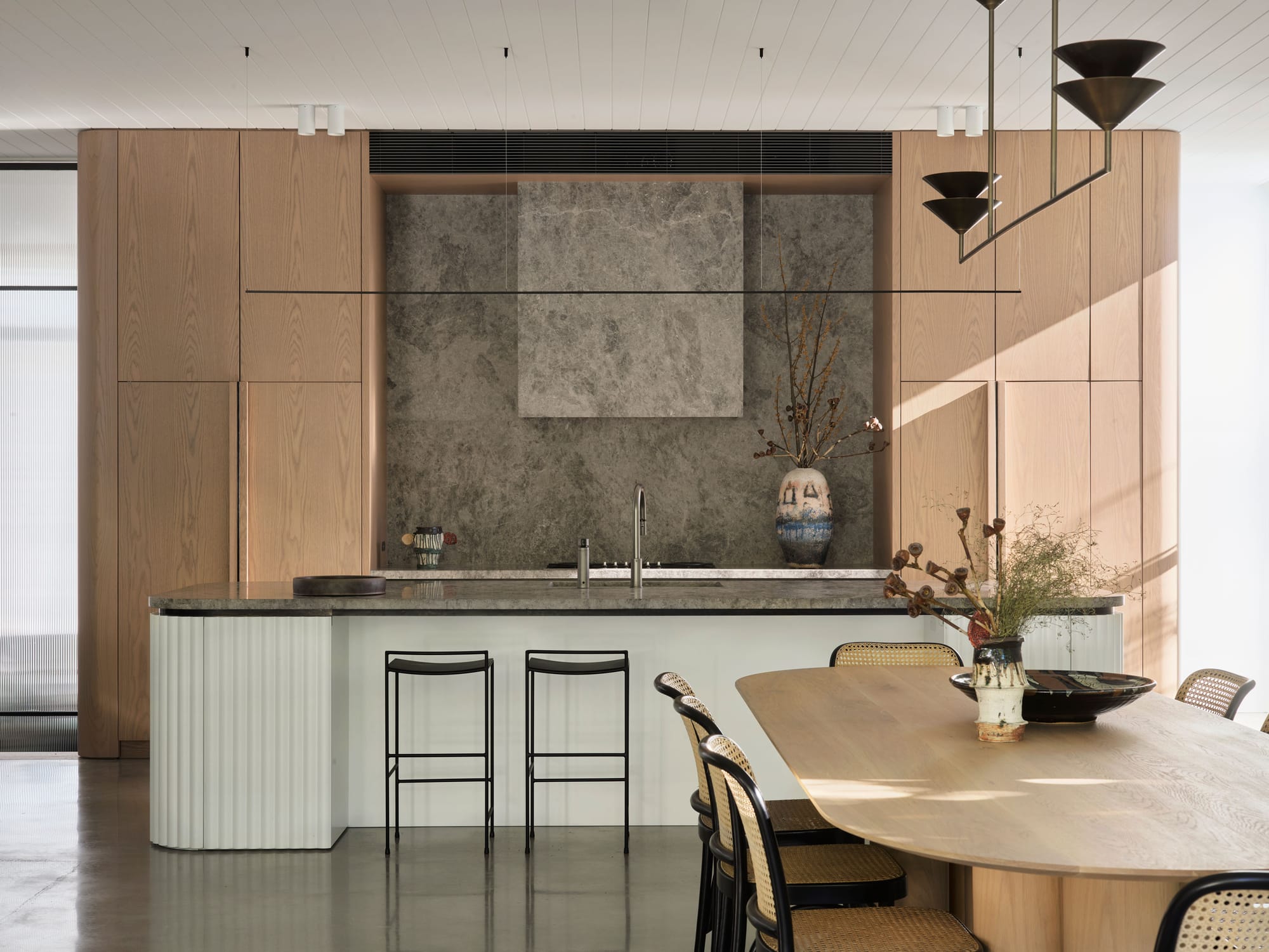 Warren House by CM Studio. Photography by Nic Gossage. Timber cabinetry in kitchen with white island bench. Grey stone splashback and countertops. 