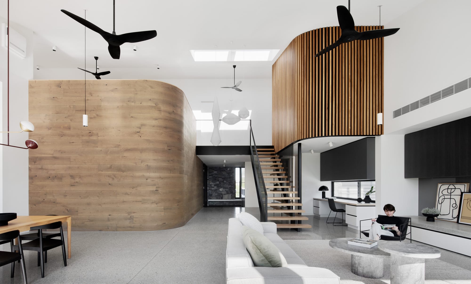 Kenny Street Huse by Chan Architecture. Photography by Tatjana Plitt.  Open plan living, dining and study area with polished concrete floors. Floating, curved, timber clad wall hangs over void above study area. 