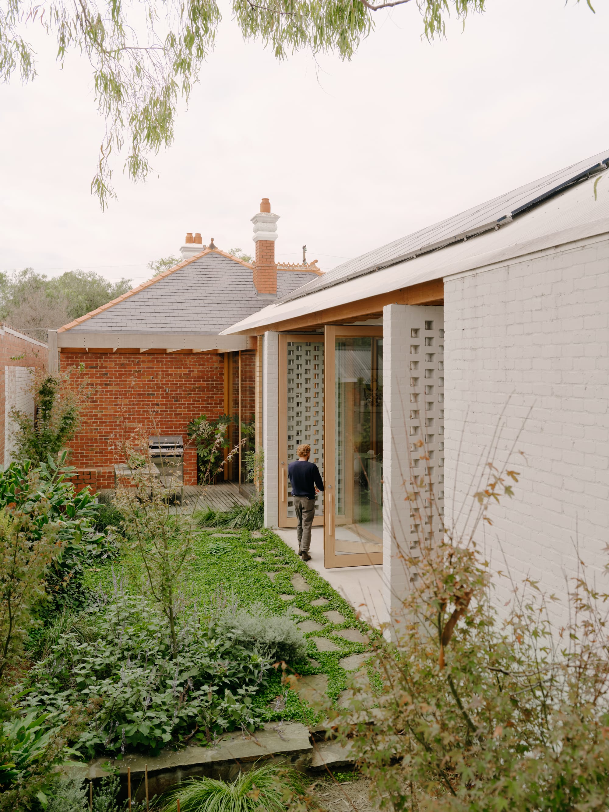 Corymbia by Karen Abernethy Architects. Photography by Tom Ross. Garden of residential home and outdoor area. Brick walls, timber deck at end of garden. Green grass and wild shrubs. 