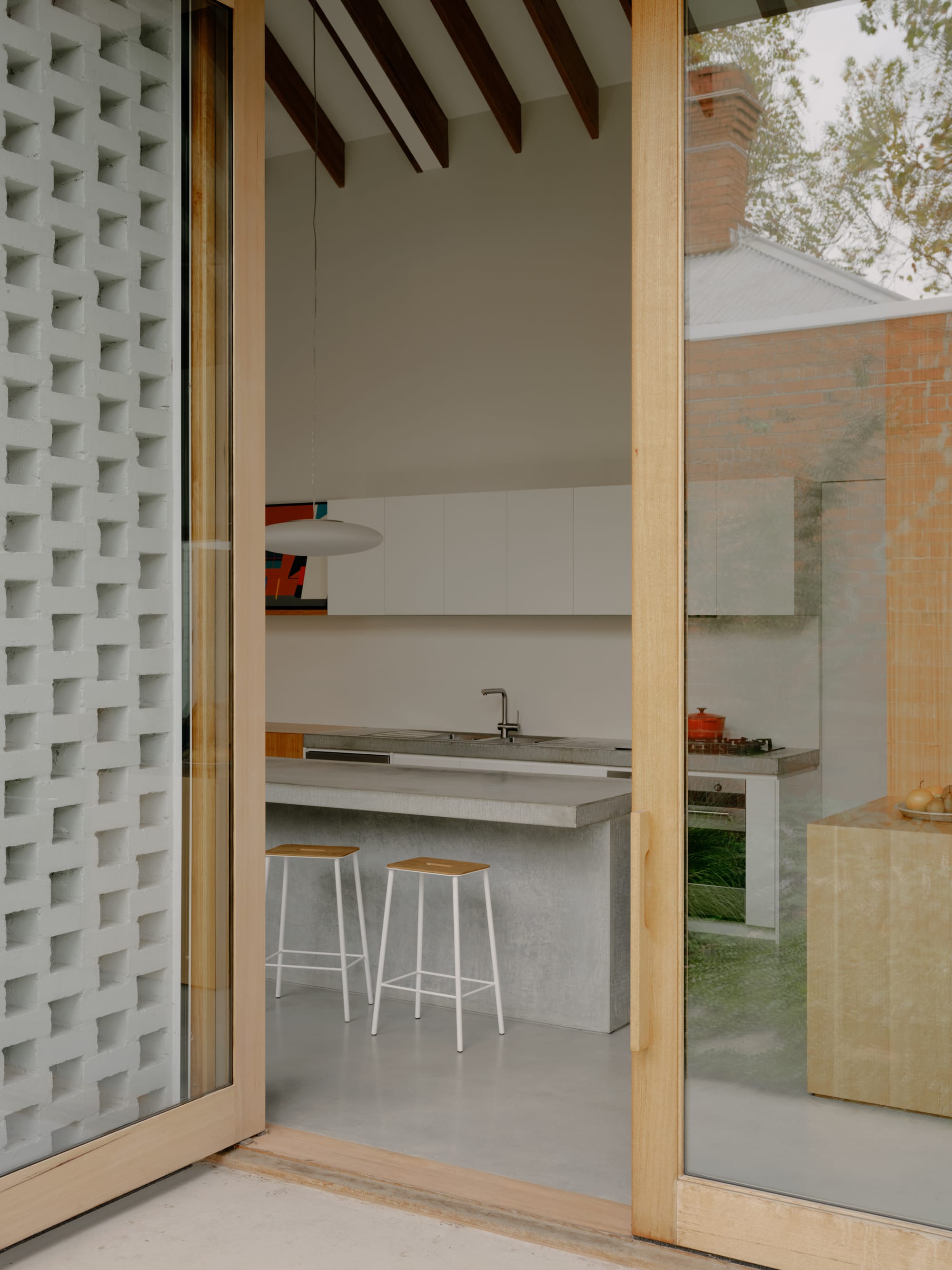 Corymbia by Karen Abernethy Architects. Photography by Tom Ross. Timber framed glass door leading from kitchen to outside area. Concrete floors and benches inside. 
