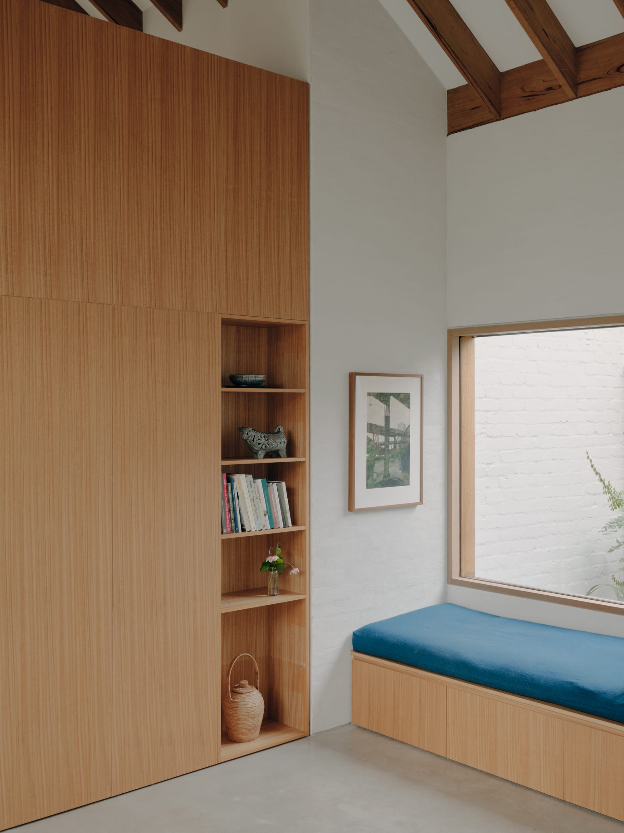 Corymbia by Karen Abernethy Architects. Photography by Tom Ross. Timber floor-to-ceiling storage on left wall and timber bench seat with blue cushion underneath window on the right. 