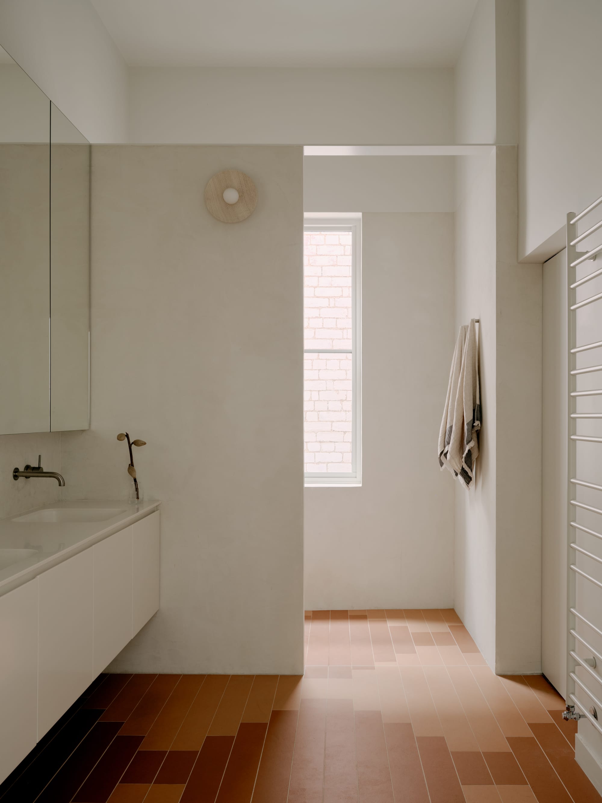 Corymbia by Karen Abernethy Architects. Photography by Tom Ross. Bathroom with patterned terracotta floor tiles and white plaster walls. White floating basin and wall mirror. 