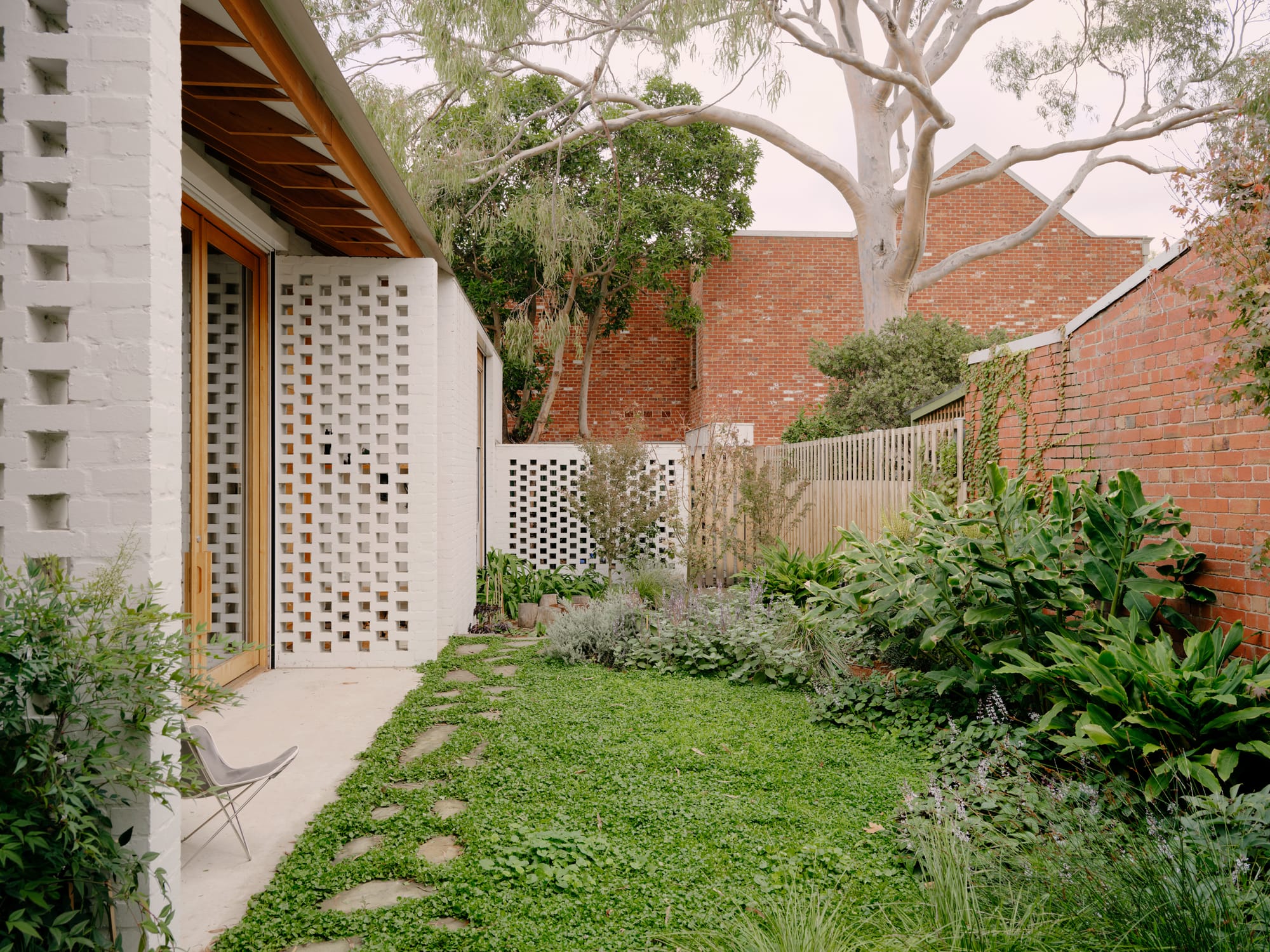 Corymbia by Karen Abernethy Architects. Photography by Tom Ross. Exterior facade of white brick home and adjoining garden. Green grass and wild shrubs to right of image. 