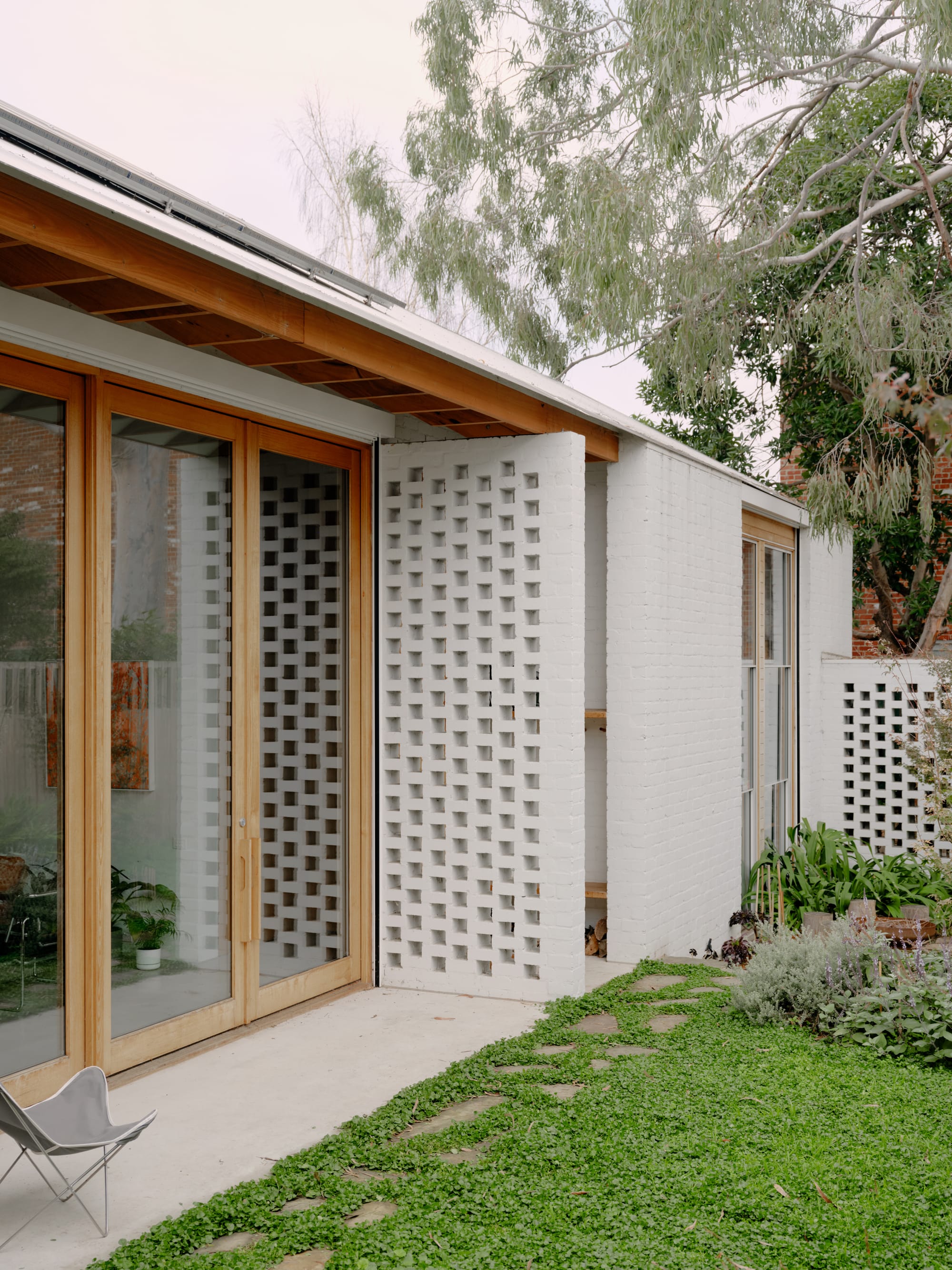 Corymbia by Karen Abernethy Architects. Photography by Tom Ross. Externa wall of residential home built from white brick. Timber framed glass doors and brick breezeblocks. Green grass. 