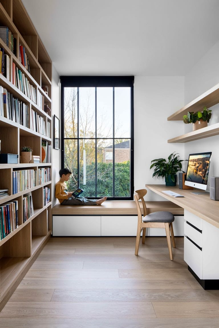 Dickens Street Residence by Chan Architecture. Photography by Tatjana Plitt. Residential office space with integrated bench seating in front of window. Floor-to-ceiling bookshelves on left hand side and integrated floating desk to right. 