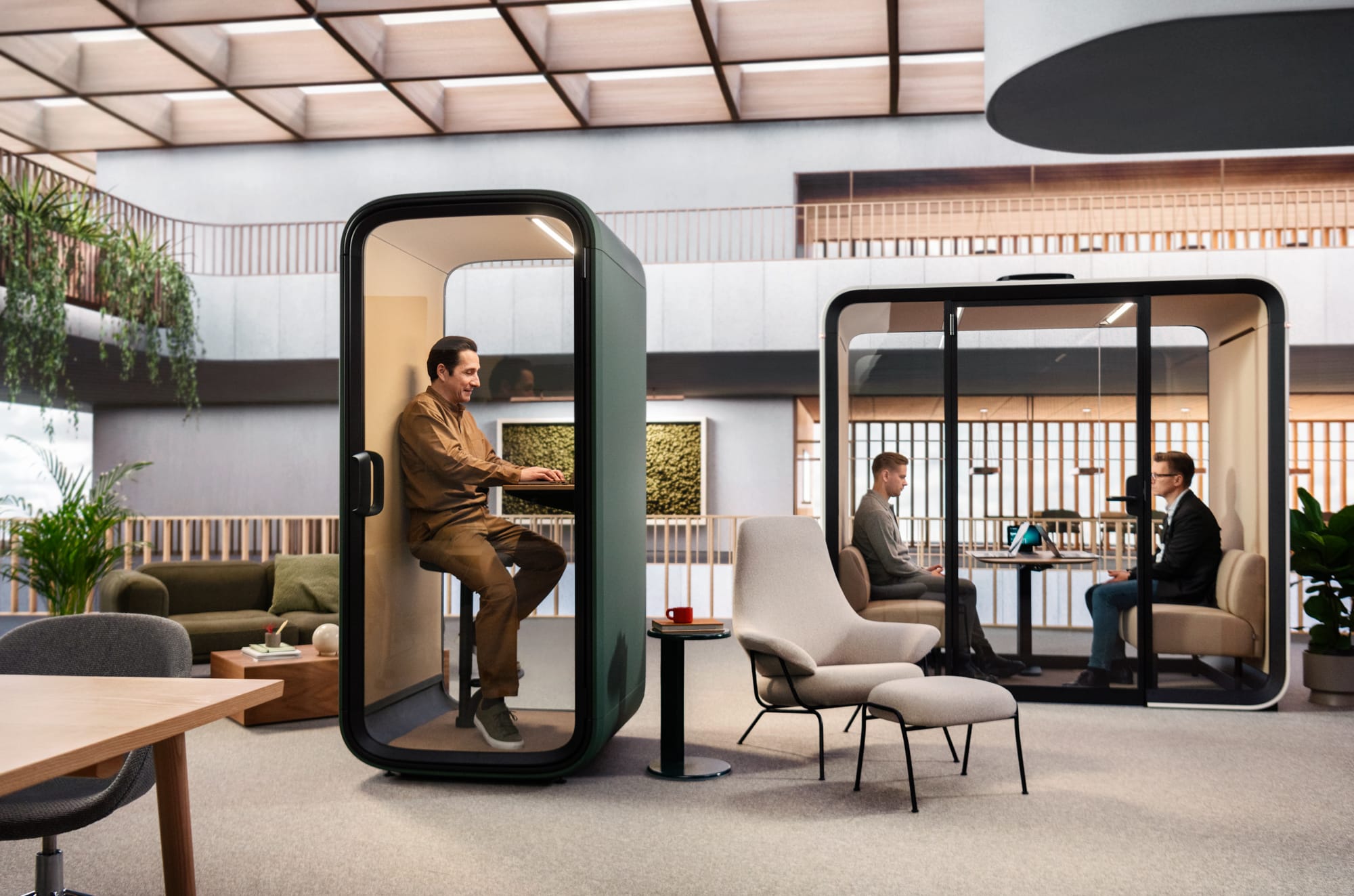 Framery Smart Pod. Copyright of Framery. Man sitting in green work pod. Two men having a meeting in work pod to the right in the background. 