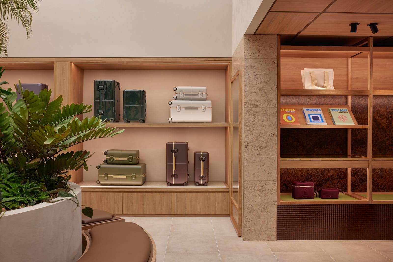 July Store by Acre. Photography by Cieran Murphy. Retail store with grey tiled floors and timber shelving. Array of coloured suitcases and books on shelves. Planter to left. 