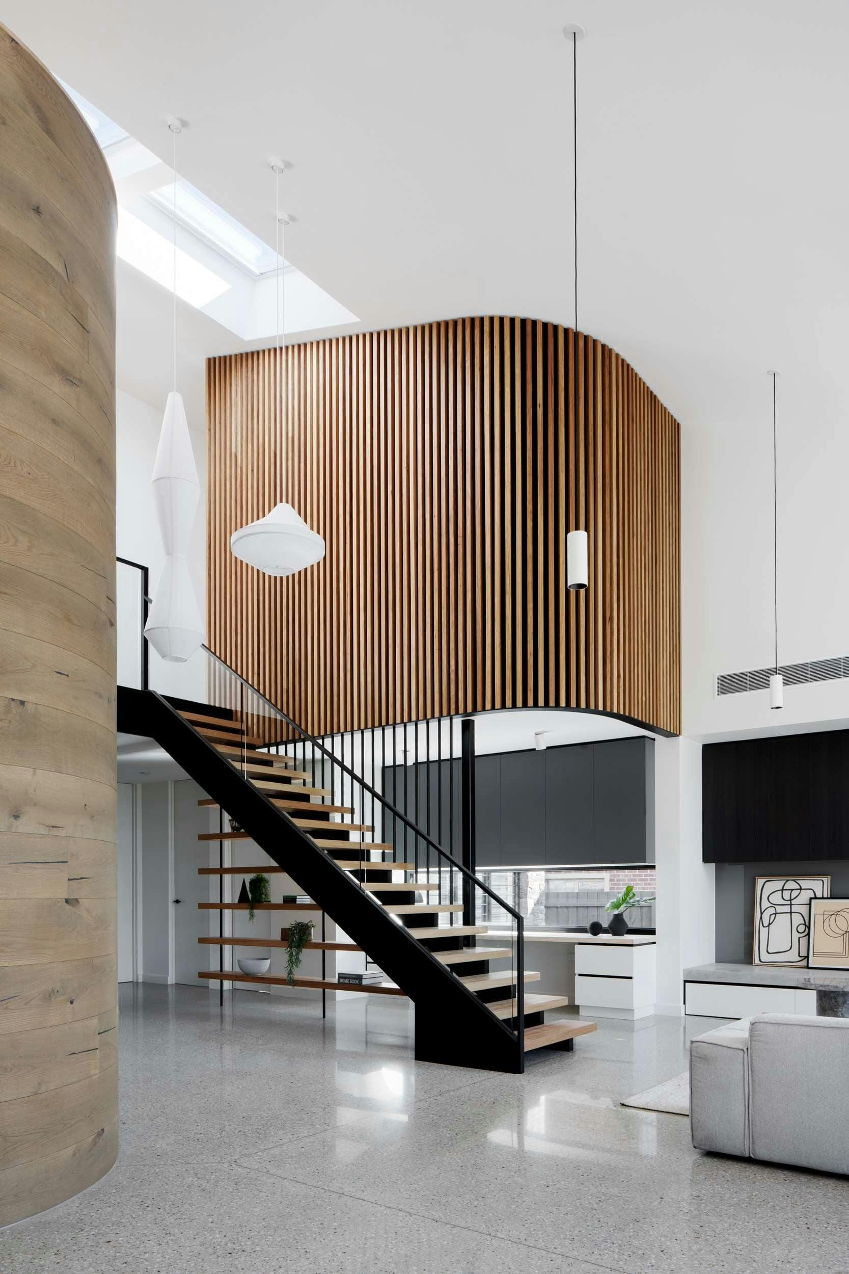 Kenny Street Huse by Chan Architecture. Photography by Tatjana Plitt. Open plan living and kitchen with central timber and metal staircase. Decorative timber clad wall on second floor floats in void above kitchen. 