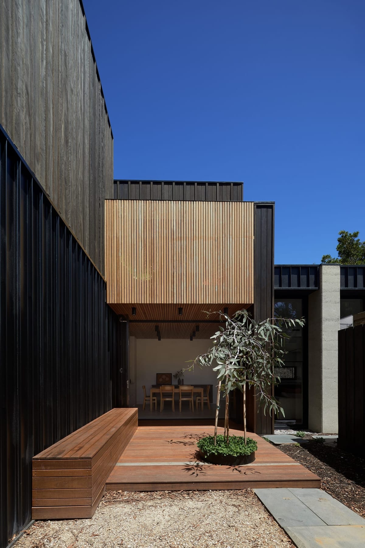 Outdoor deck opening out from interior dining space. Black timber clad walls and bench seating. 