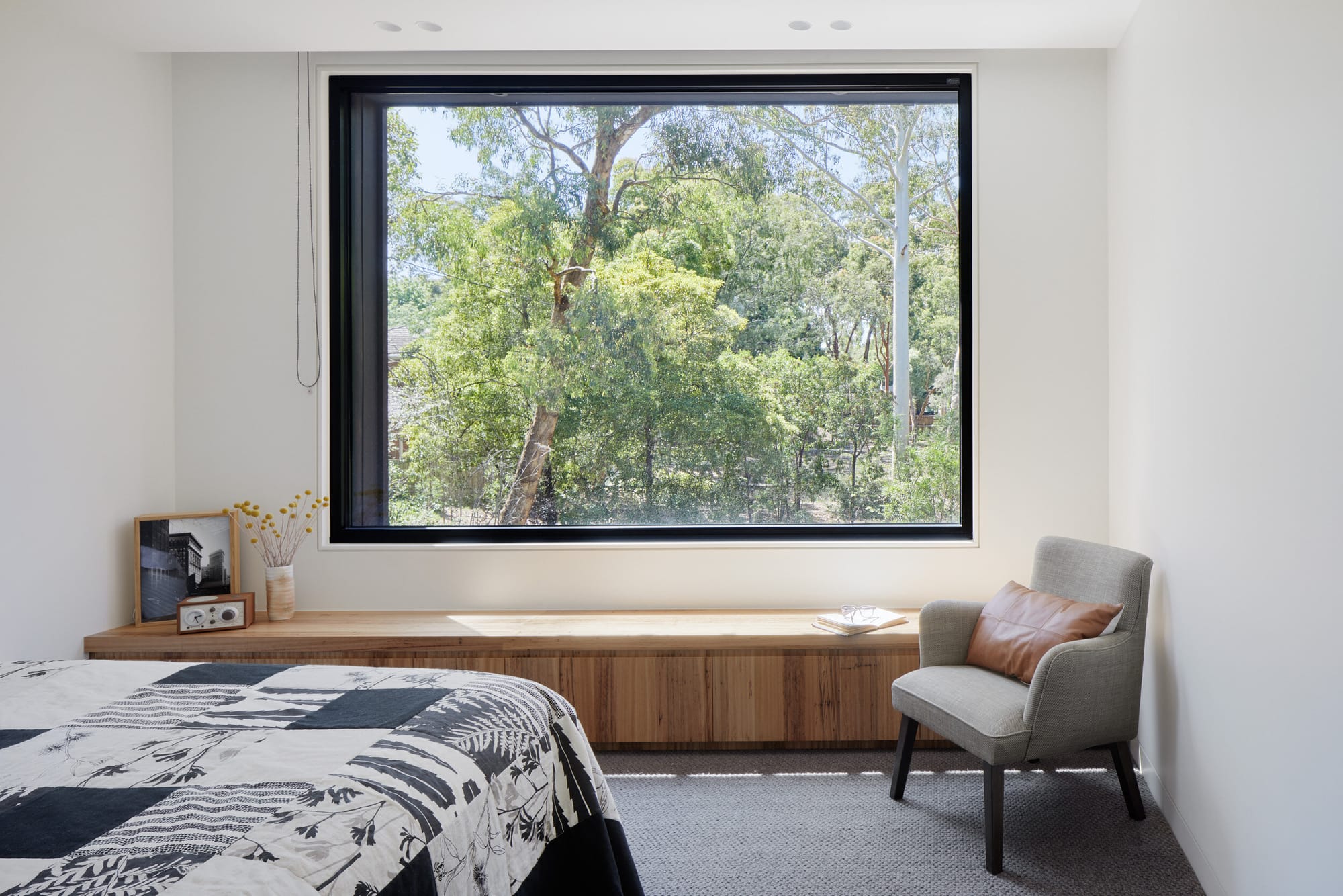 Laurel Grove by Kirsten Johnstone Architecture. Photography by Tatjana Plitt. Upstairs bedroom with built in timber bench running length of wall. Window overlooks gum trees.