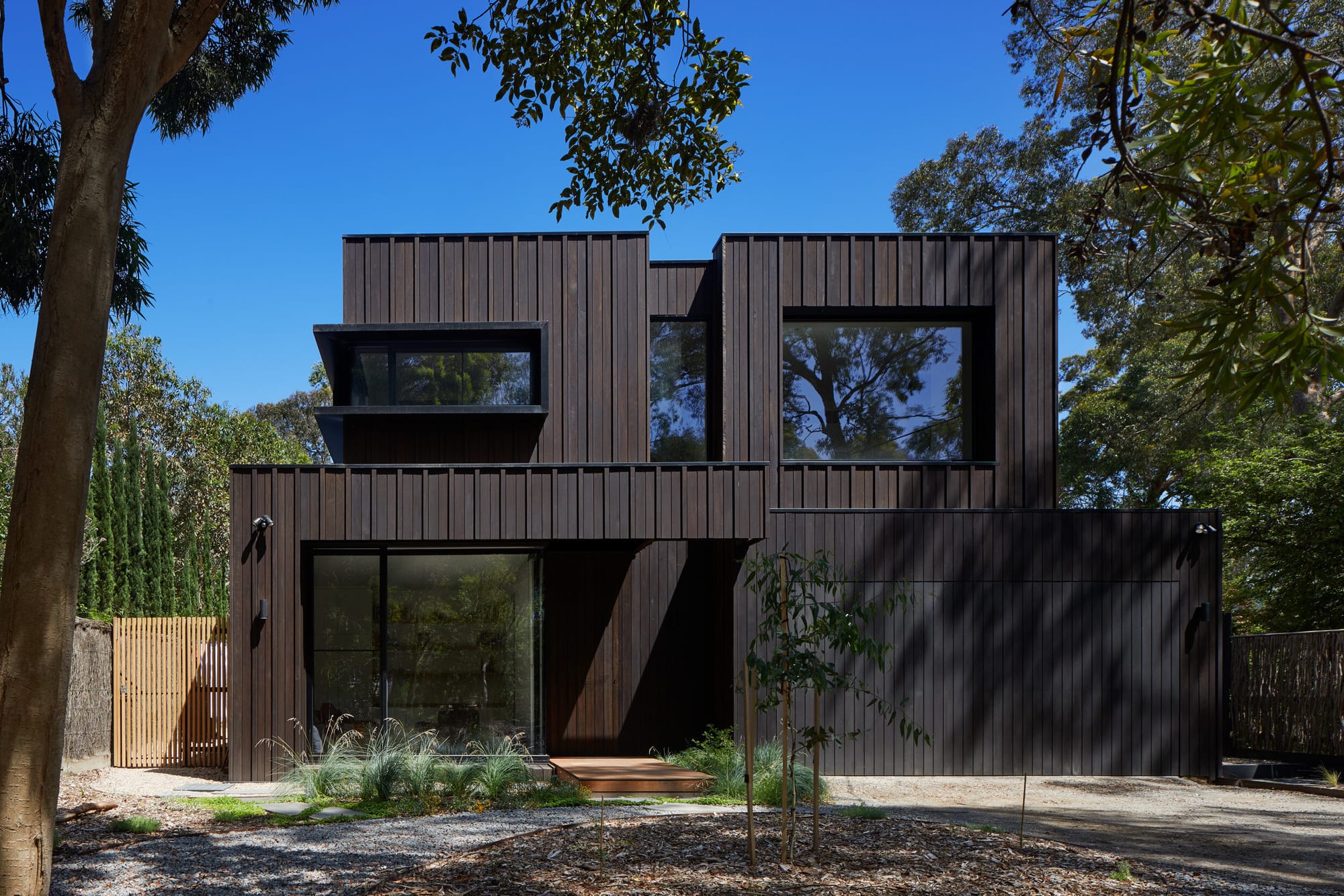 Laurel Grove by Kirsten Johnstone Architecture. Photography by Tatjana Plitt. Street facade of contemporary two storey home clad in black timber. Sparse natural gardens around home.