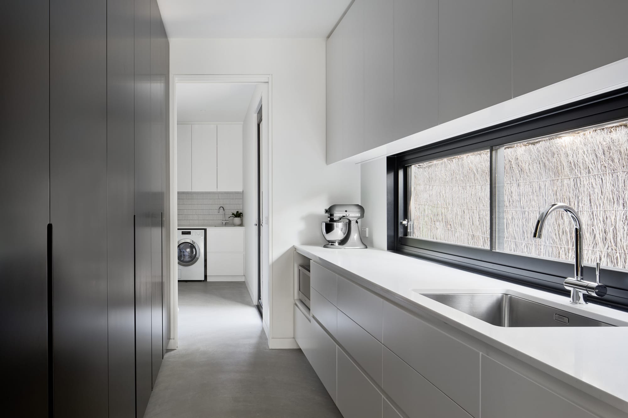 Laurel Grove by Kirsten Johnstone Architecture. Photography by Tatjana Plitt. Scullery space with white and black counters and storage. Polished concrete floors.