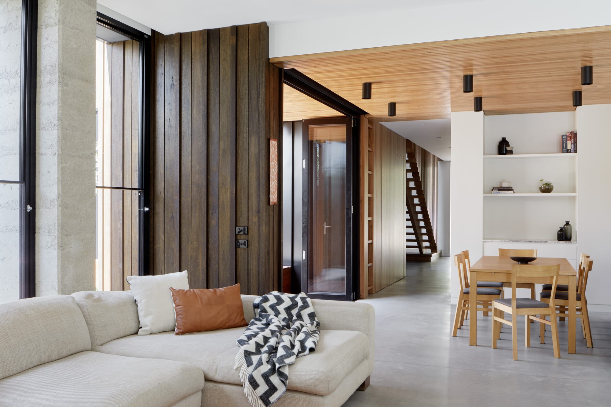 Laurel Grove by Kirsten Johnstone Architecture. Photography by Tatjana Plitt. Open plan living and dining area with polished concrete floor. Timber ceiling, wall and staircase in background.