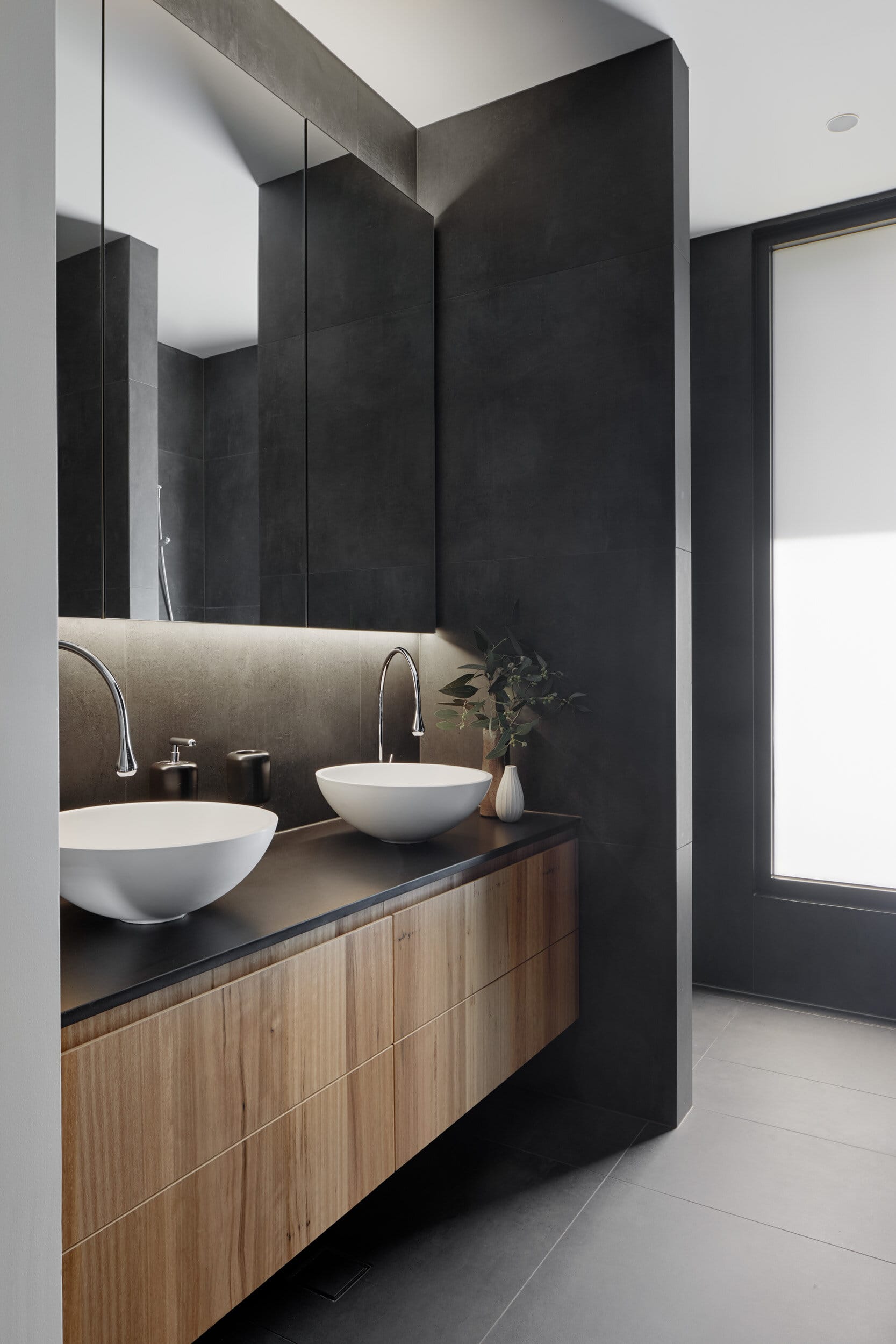 Laurel Grove by Kirsten Johnstone Architecture. Photography by Tatjana Plitt. Timber bathroom vanity with black countertop and two freestanding sink bowls. Dark walls and mirrors.