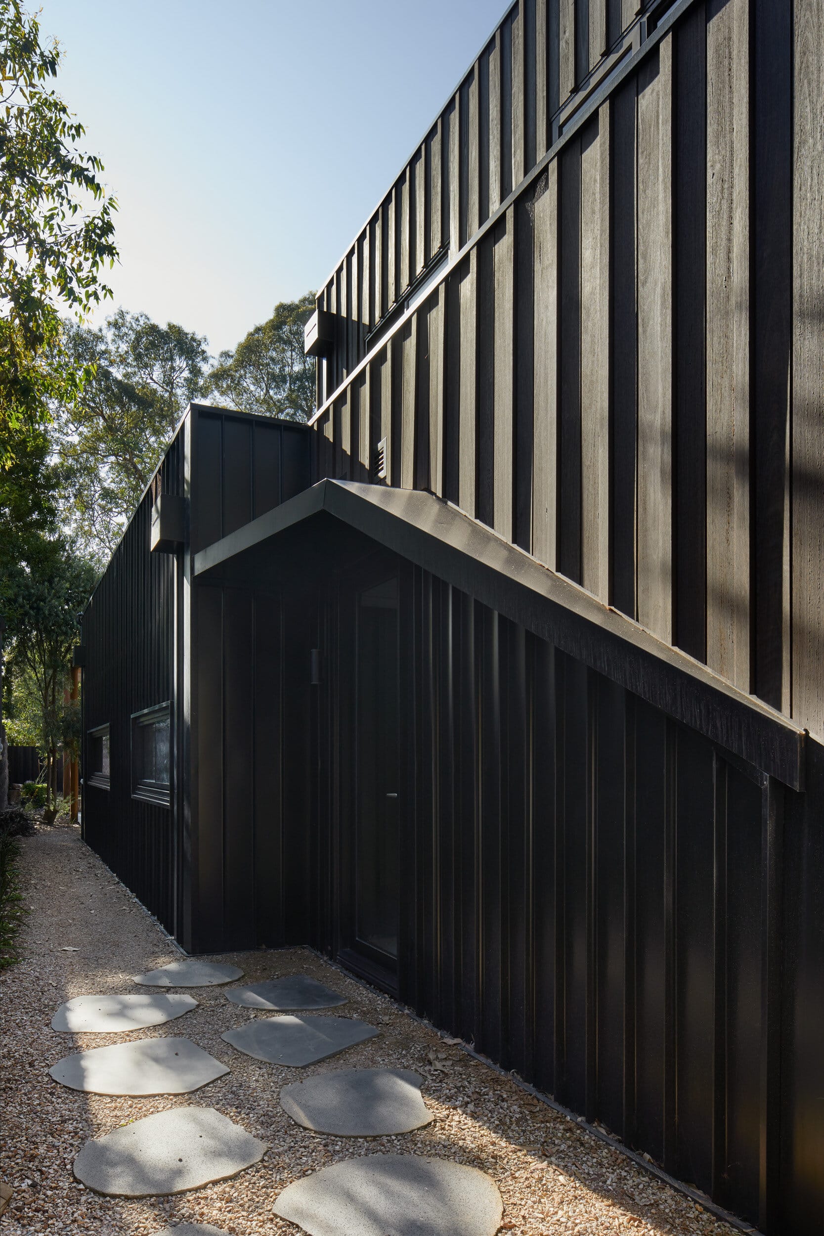 Laurel Grove by Kirsten Johnstone Architecture. Photography by Tatjana Plitt. Side of contemporary home clad in black timber. Paver footpath leading to side door. 