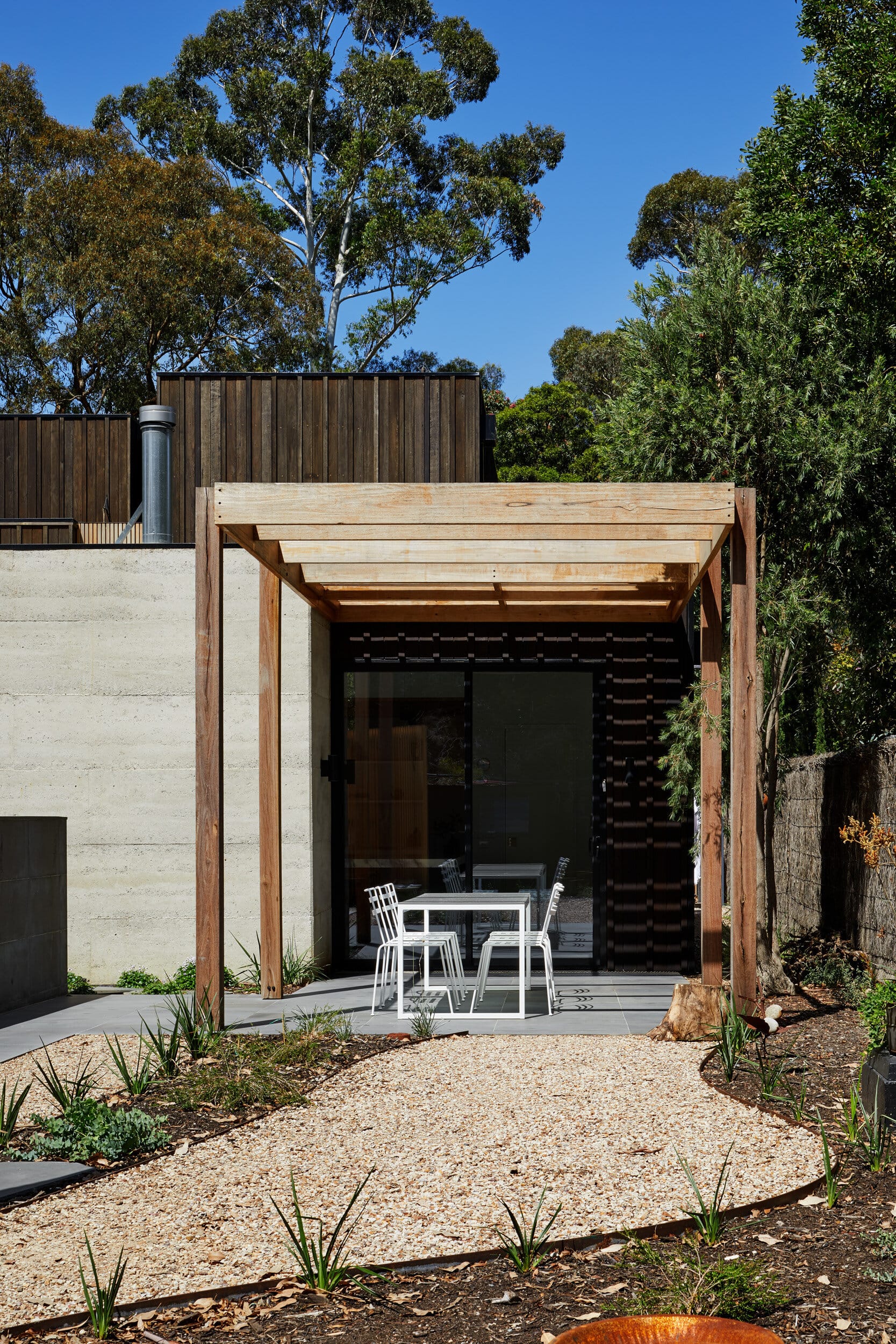 Laurel Grove by Kirsten Johnstone Architecture. Photography by Tatjana Plitt. Outdoor pation with concrete floor and timber pergola. Garden landscaped with stones, plants and pathways.