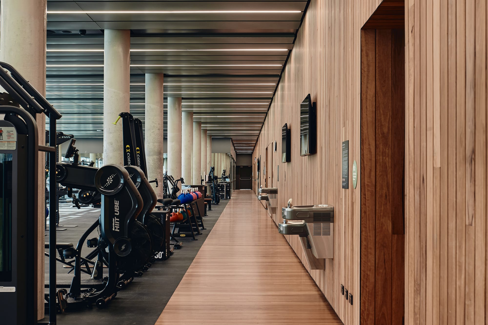 Parramatta Aquatic Centre by Mortlock Timbers. Photography by Peter Bennetts. Indoor gym with walkway running down the right hand wall. Timber floors and walls on walkway. 