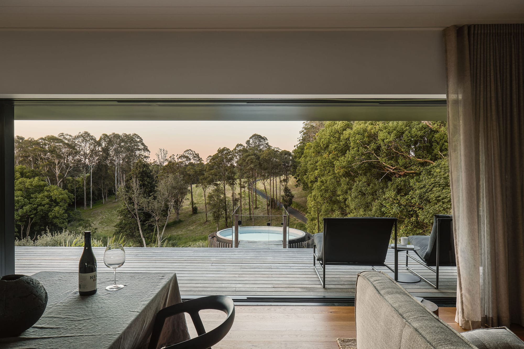 Rockpool Farm Byron Bay. Photography by Andy Macpherson. Large window opening from open plan living and dining area with timber floors onto timber deck. Round pool extending from deck. Hillside views. 