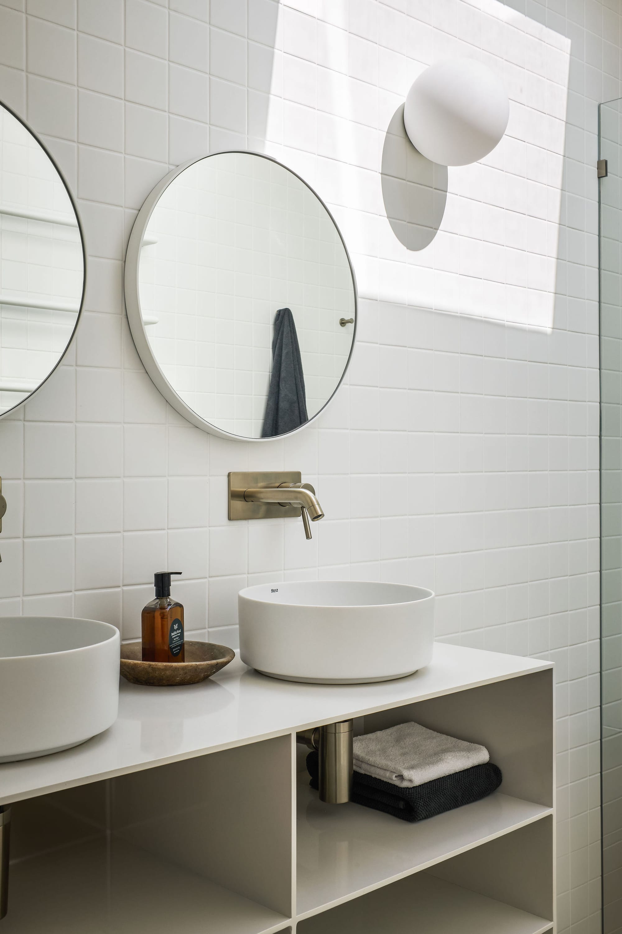 Rockpool Farm Byron Bay. Photography by Andy Macpherson. White tiled bathroom wall with white vanity. Open faced storage and round matching sinks. Round wall hung mirrors.